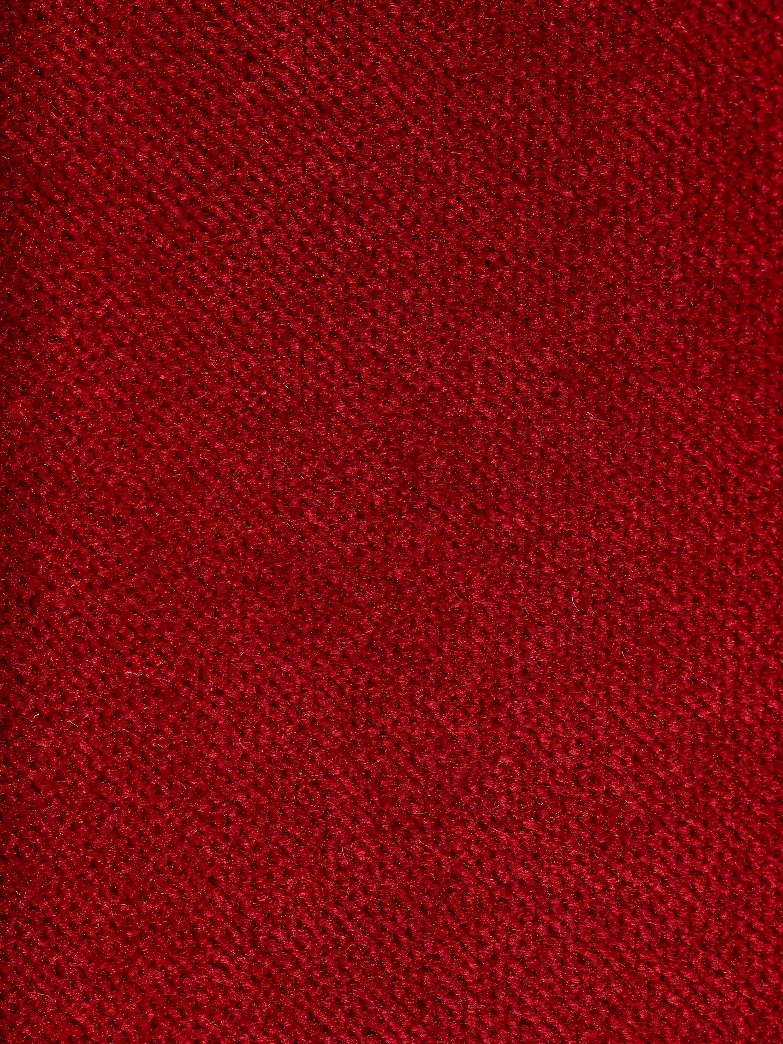 Primo piano del raffinato rivestimento in tessuto effetto velluto smacchiabile T30 in un rosso intenso, che presenta una trama morbida e leggermente felpata con un delicato motivo intrecciato. Il gioco di luci e ombre sulla superficie ne esalta la profondità e il fascino visivo, riflettendo la raffinata maestria artigianale italiana del divano letto di design Capri con piedini alti e poggiatesta reclinabili di Divani.Store.