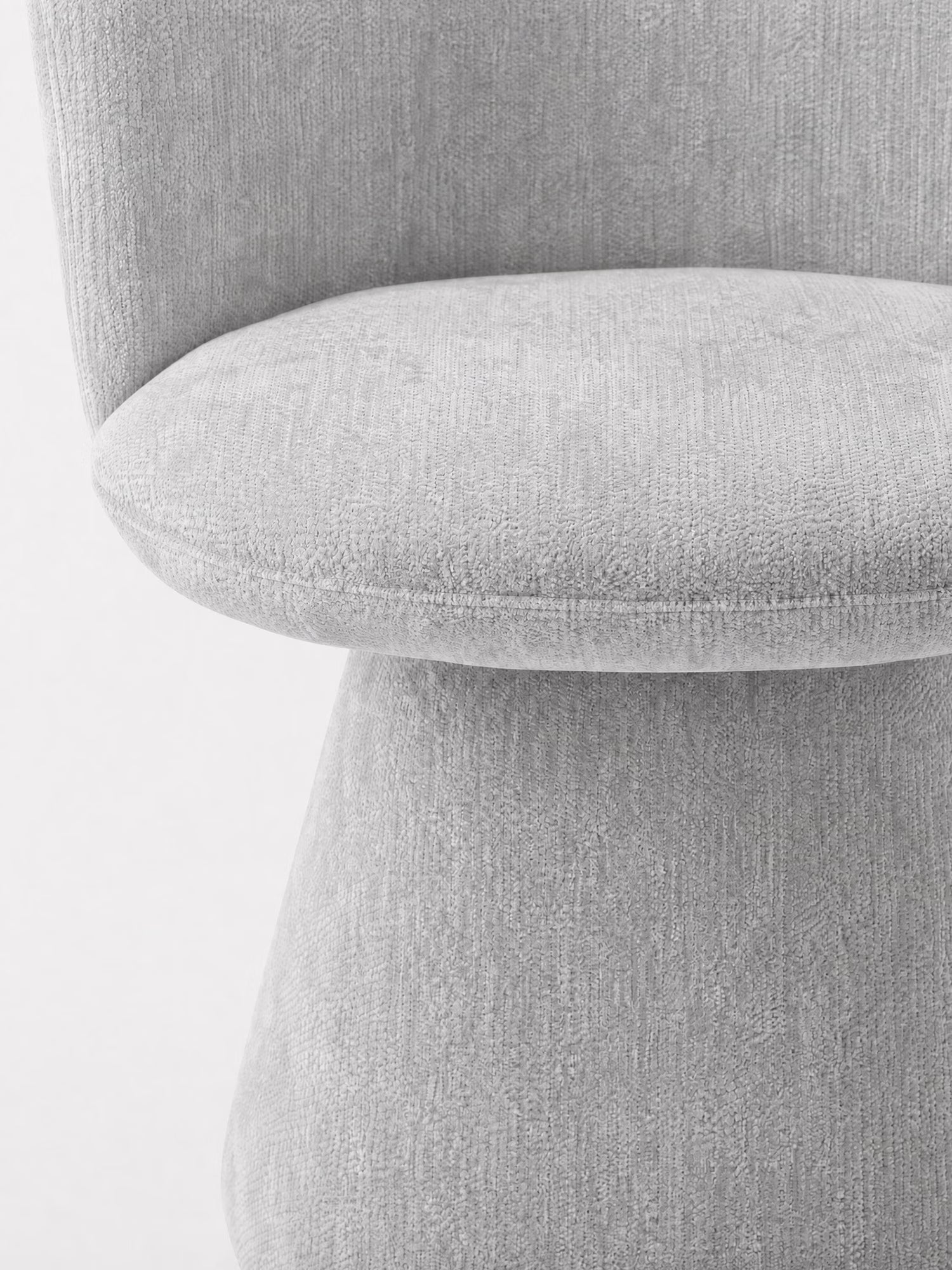 Primo piano della sedia moderna imbottita Talia di Divani.Store, rivestita in ciniglia grigio chiaro certificata OEKO-TEX®. L'immagine mostra la seduta curva e lo schienale basso, caratterizzati da un tessuto morbido e da un design minimalista, su uno sfondo bianco a tinta unita.