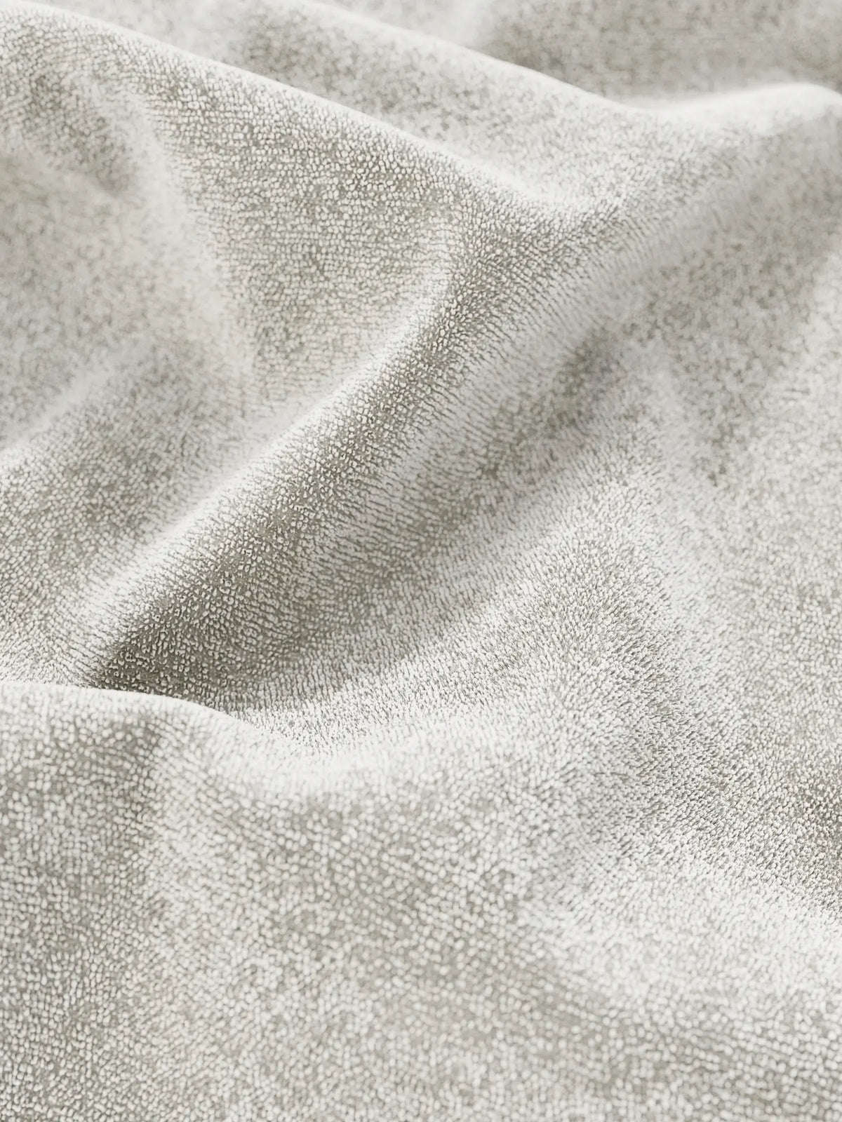 Primo piano sul morbido tessuto in ciniglia grigio chiaro certificato Oeko-Tex® del letto imbottito AURO con contenitore e testiera capitonné alta, caratterizzato da delicate pieghe e da una delicata lucentezza.