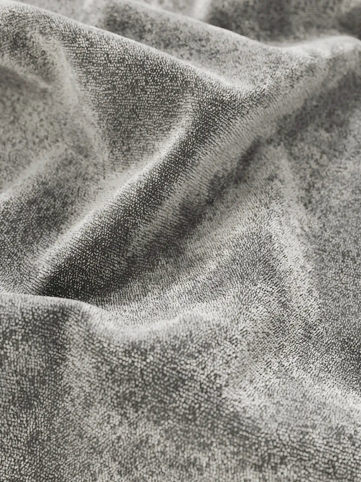 Primo piano sul morbido tessuto ciniglia grigio, dal tocco vellutato, del letto imbottito AURO con vano contenitore e testiera capitonné alta in ciniglia Oeko-Tex®, caratterizzato da profonde pieghe che creano un gioco di luci e ombre sulla sua superficie vellutata.