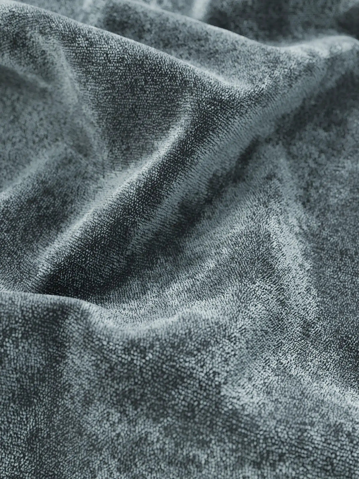 Primo piano del tessuto in velluto grigio scuro su un letto imbottito AURO con contenitore e testiera alta capitonné in ciniglia Oeko-Tex®, caratterizzato da pieghe profonde e da morbide trame screziate che creano giochi dinamici di ombre e luci.