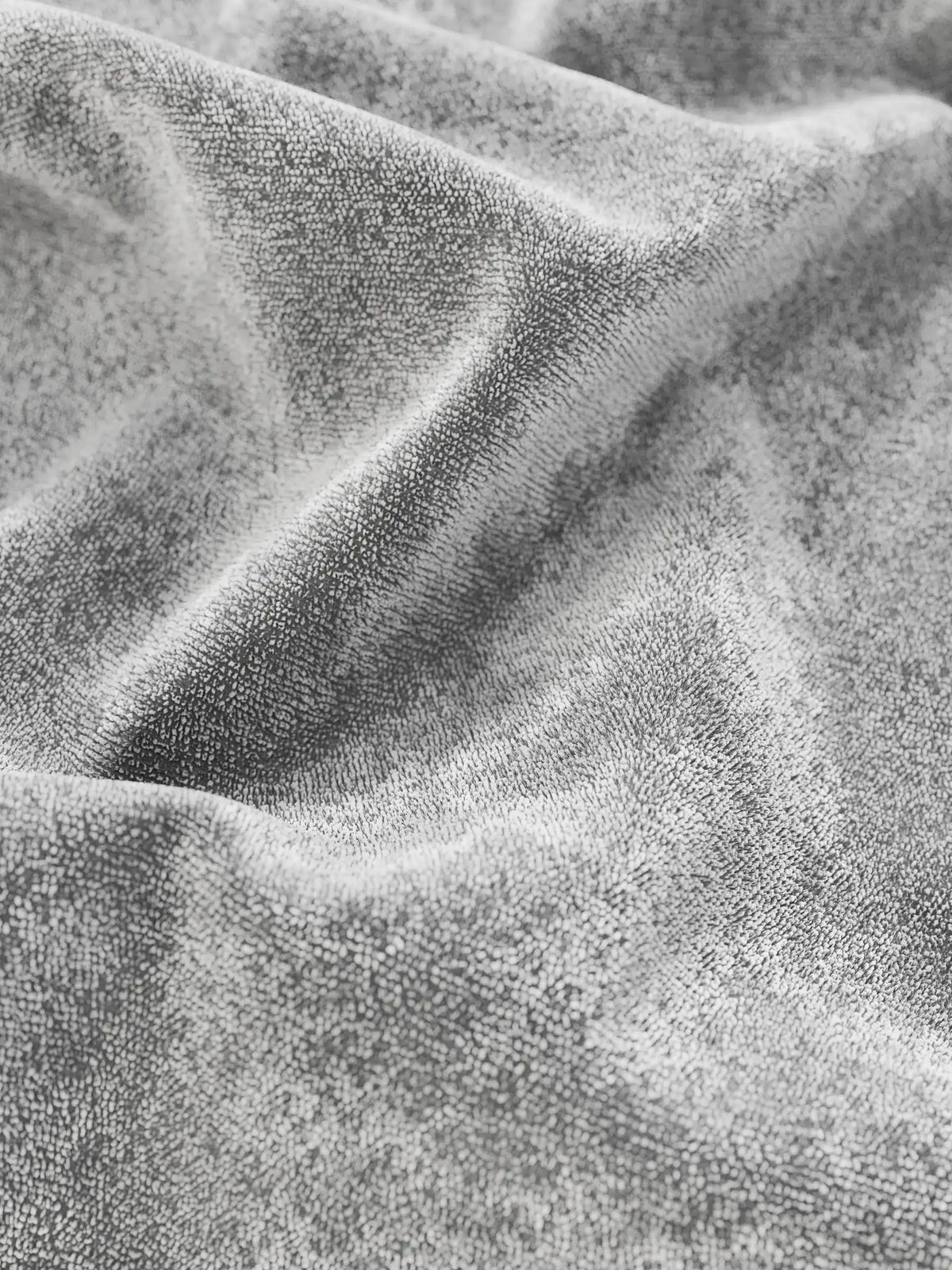 Un primo piano del letto imbottito AURO con contenitore e testiera capitonné alta in ciniglia Oeko-Tex®, caratterizzata da un morbido tessuto grigio chiaro dalla superficie soffice e ruvida, arricciato in pieghe delicate e profonde.