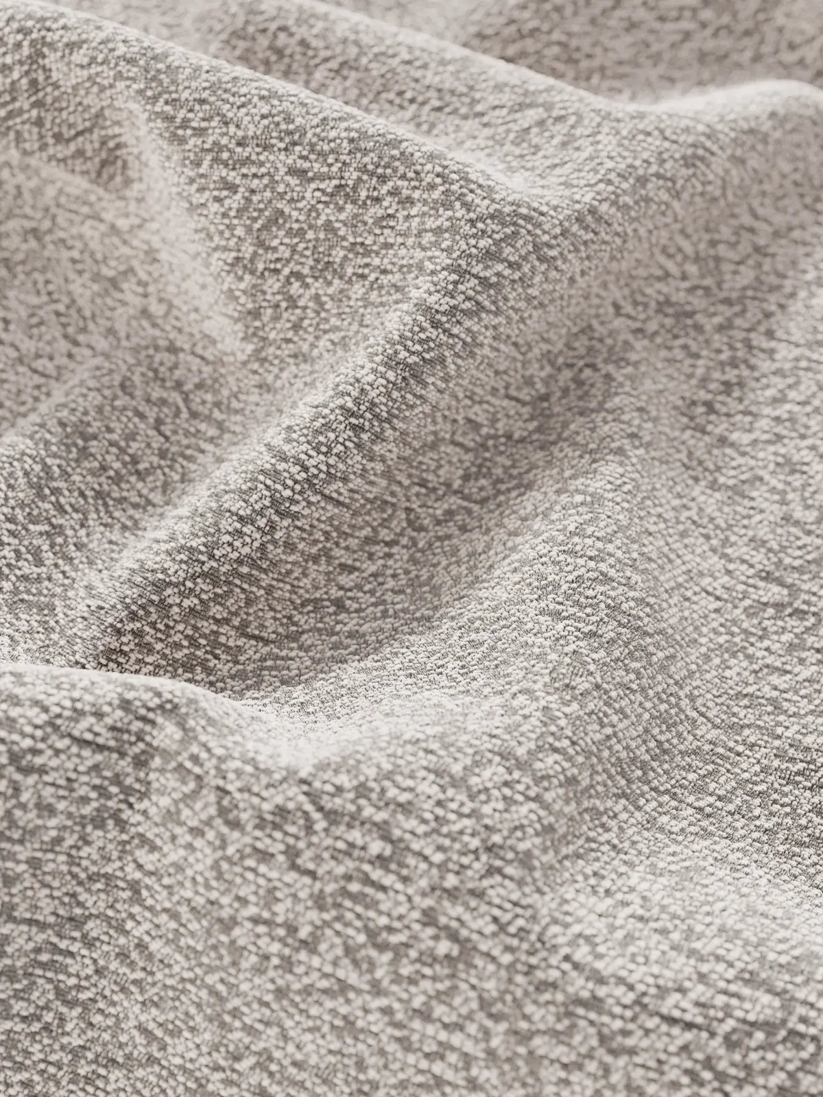 Primo piano del tessuto beige del letto imbottito ZAYRON con contenitore e morbidi cuscini regolabili, che presenta un aspetto intrecciato e testurizzato con morbide pieghe che creano sottili giochi d’ombra, mettendo in risalto la consistenza granulosa e tattile del materiale.