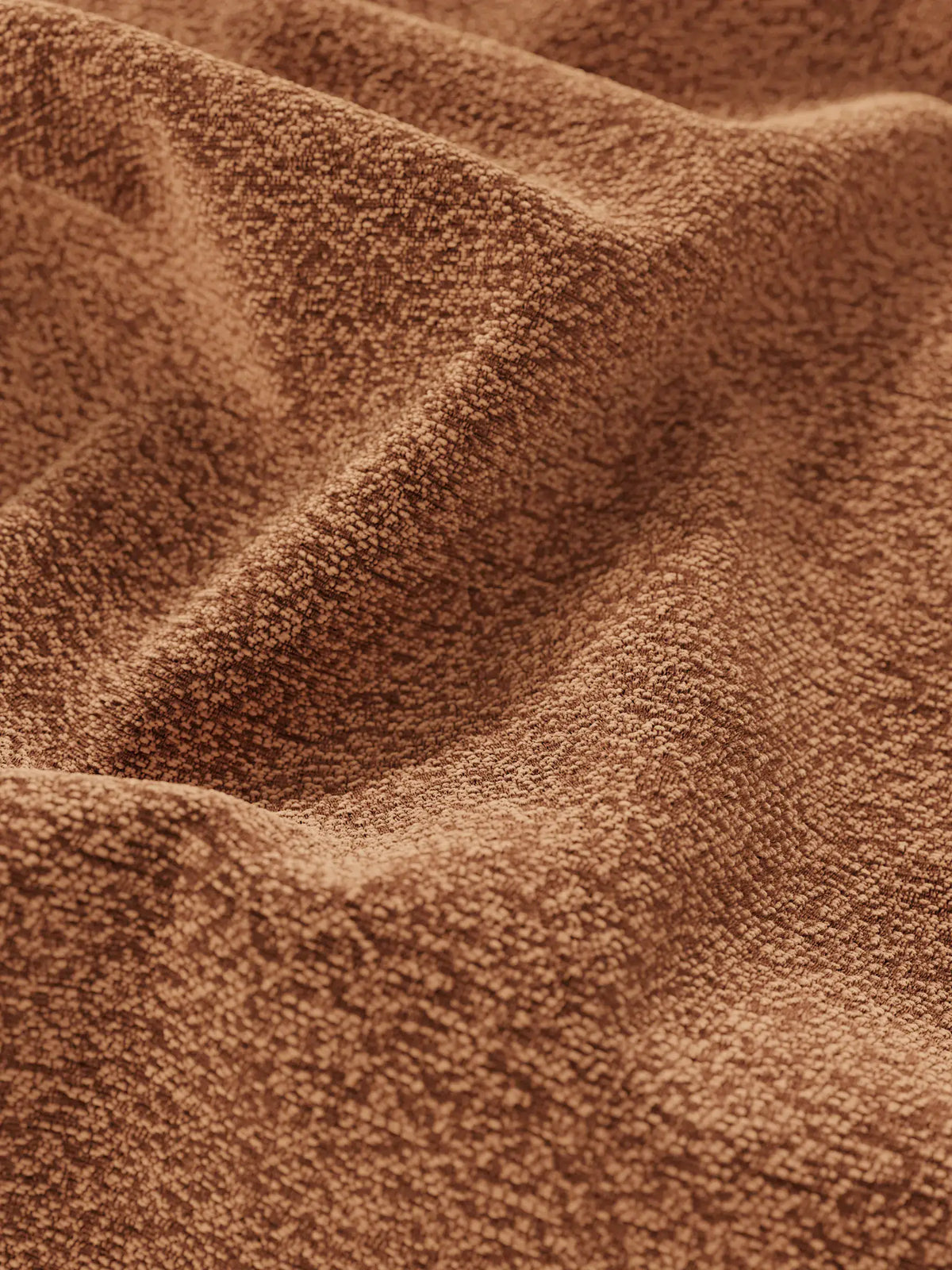 Un primo piano del tessuto testurizzato color terracotta che riveste il letto imbottito ZAYRON con vano contenitore e morbidi cuscini regolabili, che mostra una trama a nodi drappeggiata in morbide pieghe che creano sottili giochi d’ombra.