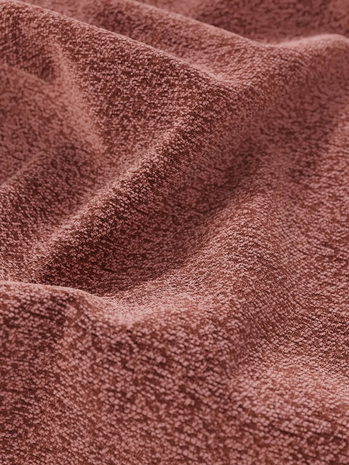 Primo piano su un tessuto color rosa polveroso su un letto di design VALKIRIA con contenitore e testiera avvolgente, drappeggiato in morbide pieghe con una trama fine e granulosa e sottili variazioni di luce e ombra.