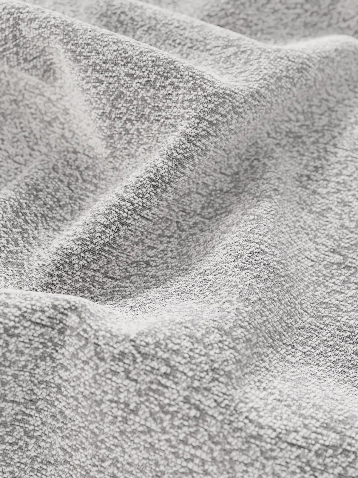 Un primo piano del tessuto grigio chiaro che riveste il letto di design VALKIRIA con contenitore e testiera avvolgente, caratterizzato da un effetto intrecciato e testurizzato, con pieghe profonde e ombre che creano increspature sulla superficie ruvida.