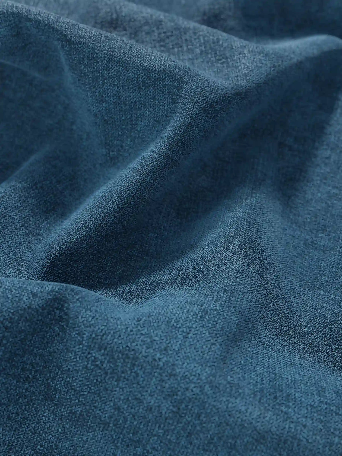 Primo piano su un tessuto intrecciato di colore blu intenso e a trama fine, che forma morbide pieghe sul letto sommier imbottito ERON con vano contenitore in tessuto impermeabile certificato Oeko-Tex, creando un delicato gioco di luci e ombre sulla sua superficie opaca.