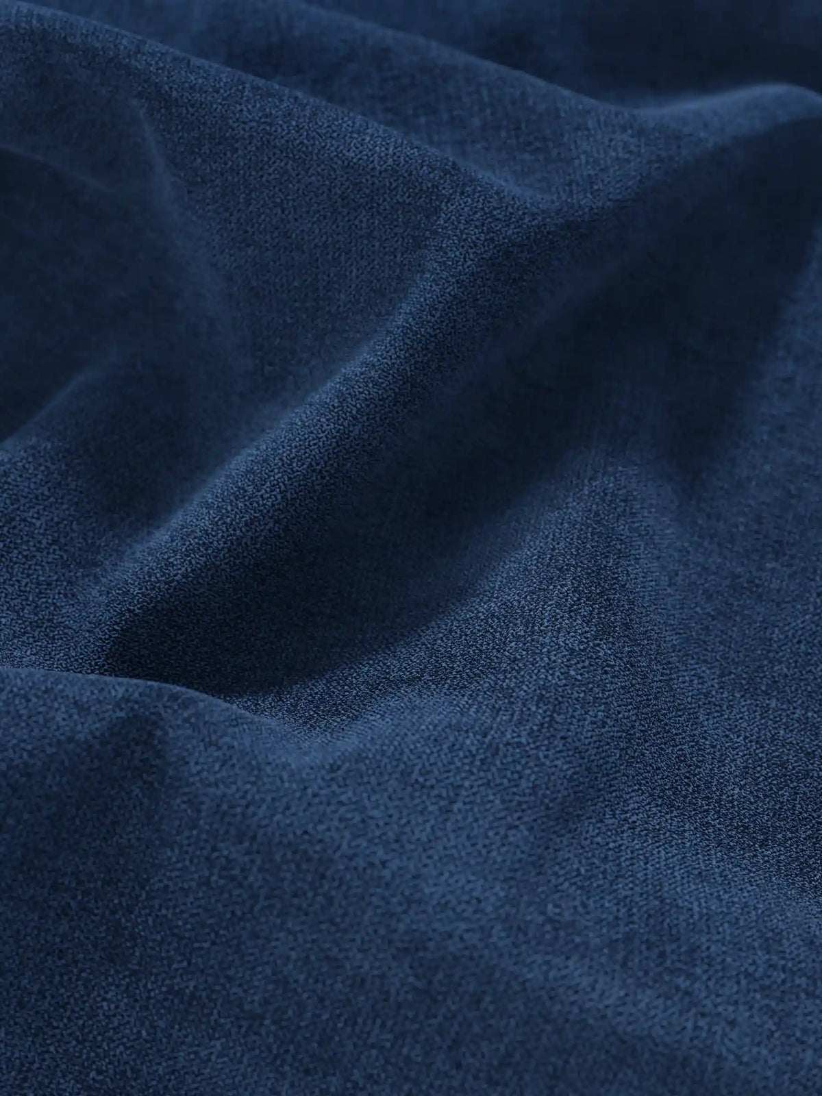 Primo piano su un tessuto blu navy intenso che riveste il letto sommier imbottito ERON con vano contenitore in tessuto impermeabile certificato Oeko-Tex, caratterizzato da morbide pieghe naturali e da una trama a grana fine che crea delicate ombre lungo le sue curve.