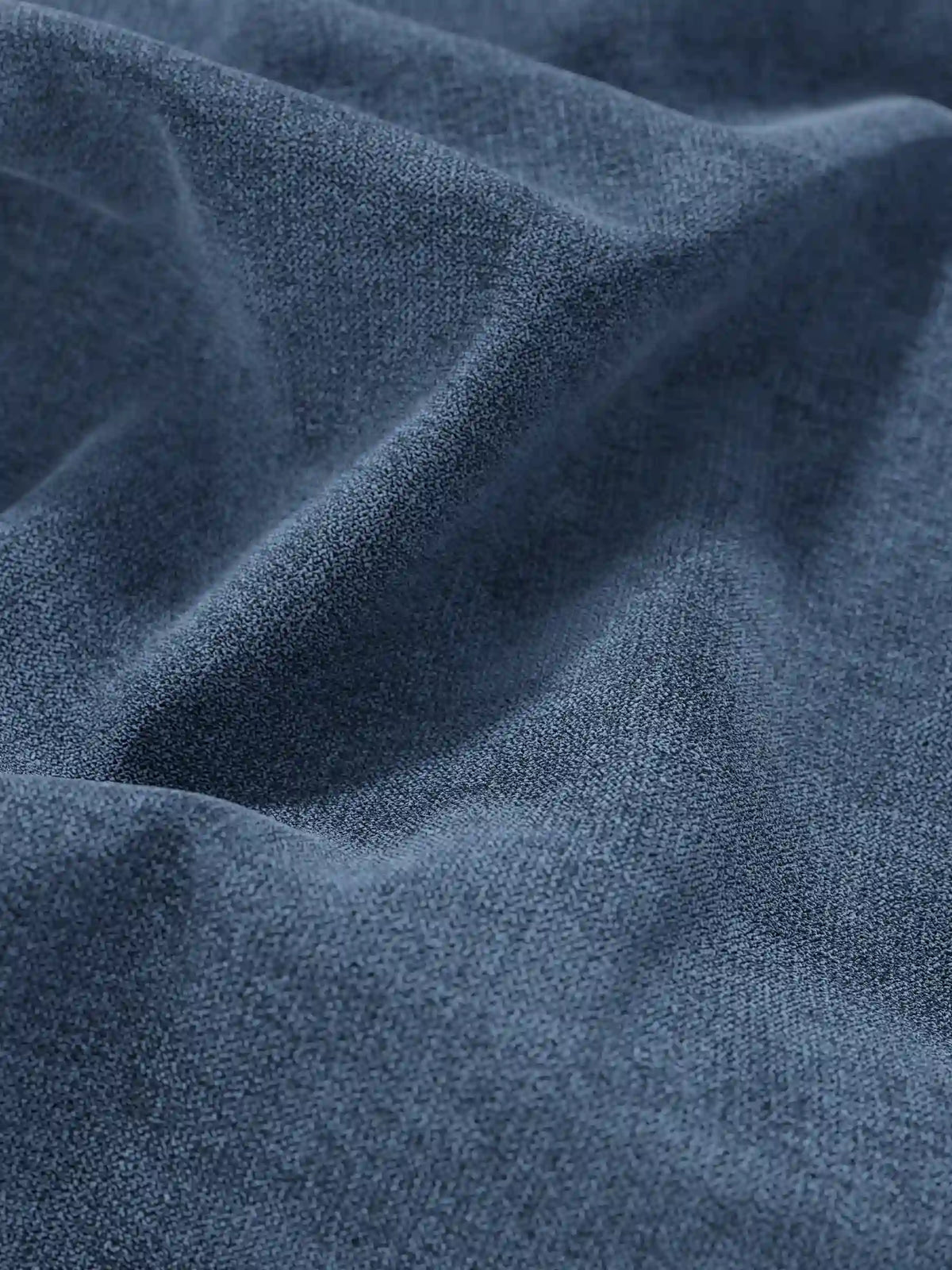 Primo piano su un tessuto blu ardesia dalla trama rigata, drappeggiato in morbide pieghe su un letto sommier ERON imbottito con vano contenitore in tessuto impermeabile certificato Oeko-Tex, con raffinati dettagli intrecciati e morbide ombre che ne esaltano la finitura opaca.