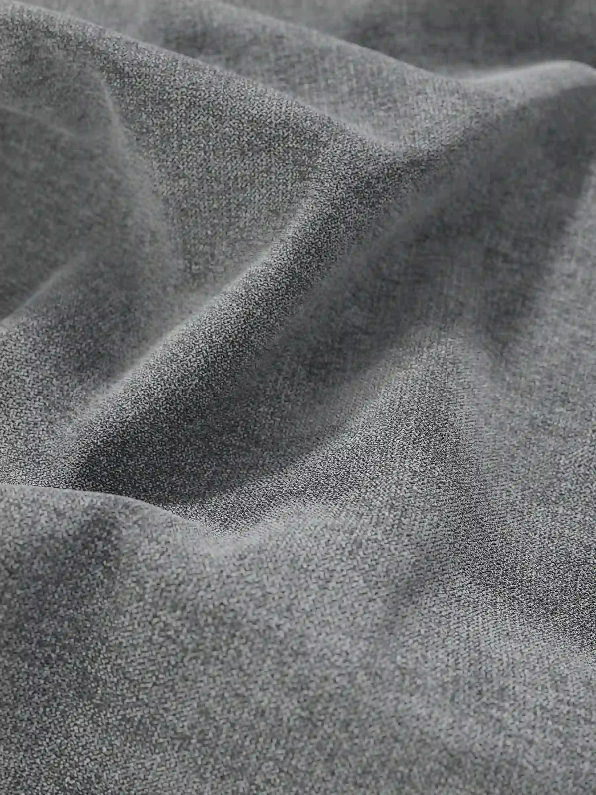 Un primo piano del letto sommier imbottito ERON grigio con vano contenitore in tessuto impermeabile certificato Oeko-Tex, che mostra morbide pieghe e una trama a grana fine con giochi di luci e ombre.