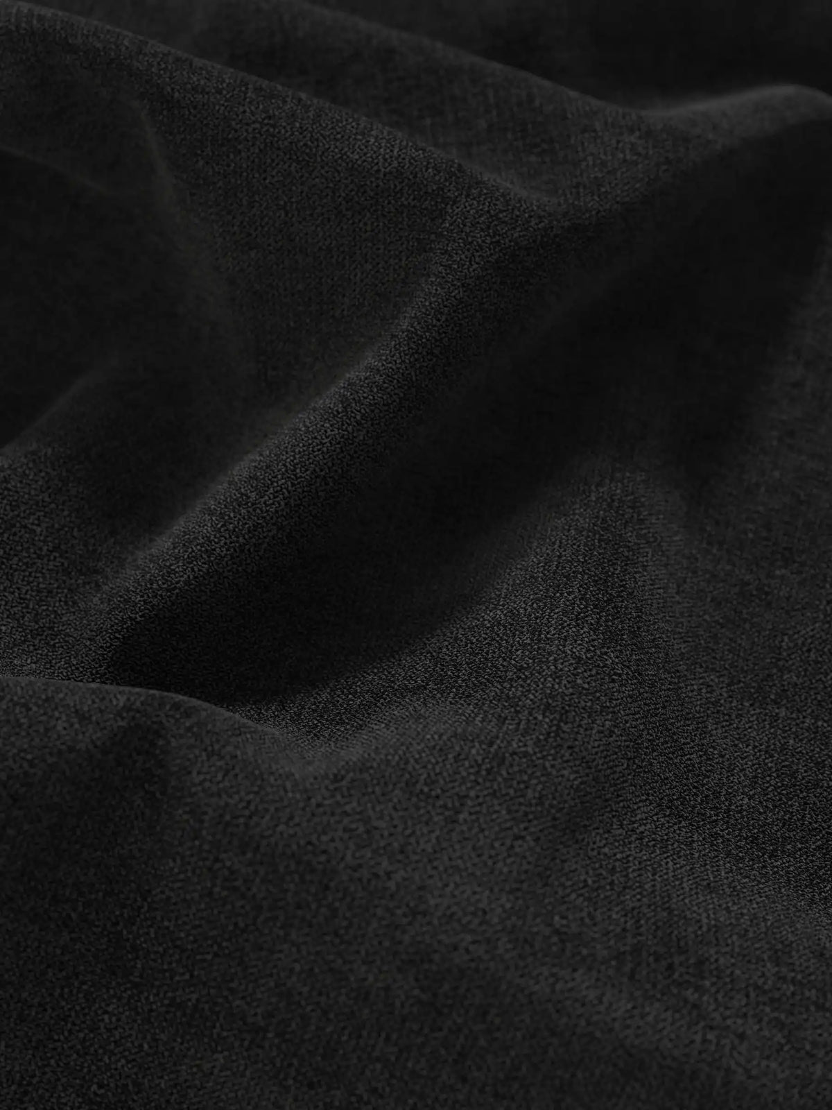 Un primo piano di un tessuto grigio scuro a trama fine su un letto sommier imbottito ERON con vano contenitore in tessuto impermeabile certificato Oeko-Tex, con morbide pieghe drappeggiate che creano sottili giochi di luci e ombre.