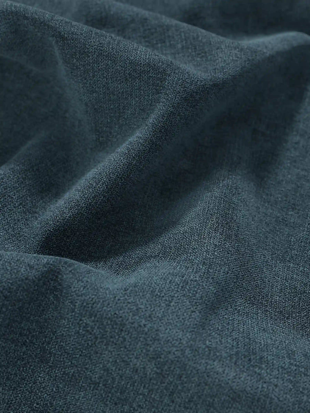 Un primo piano del tessuto color verde acqua scuro a trama fine che riveste un letto sommier imbottito ERON con vano contenitore in tessuto impermeabile certificato Oeko-Tex, con pieghe profonde che creano morbide ombre e riflessi che ne esaltano la finitura opaca.