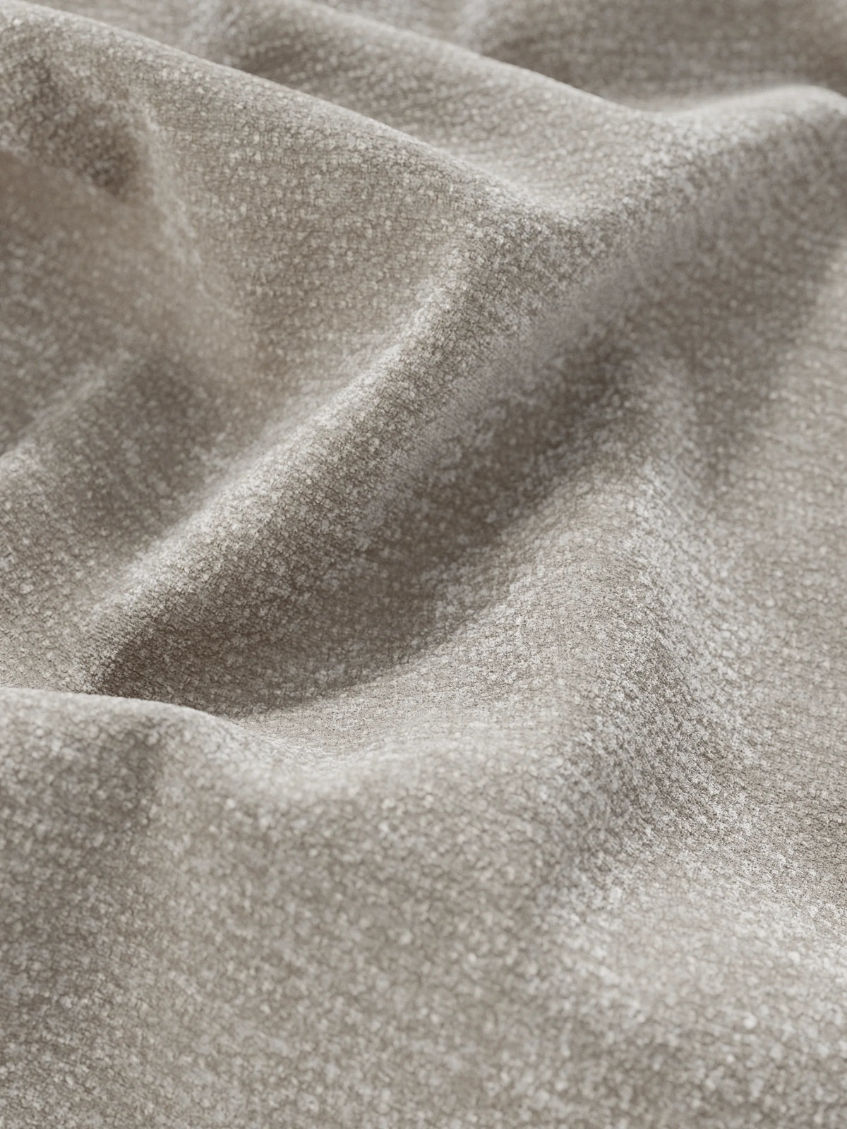 Primo piano sul tessuto in ciniglia beige a trama ruvida, che forma morbide pieghe sul letto KAELOS minimal imbottito – con vano contenitore, piedini alti e testiera arrotondata in tessuto ciniglia, caratterizzata da una superficie soffice e screziata con ombre che ne definiscono la profondità.