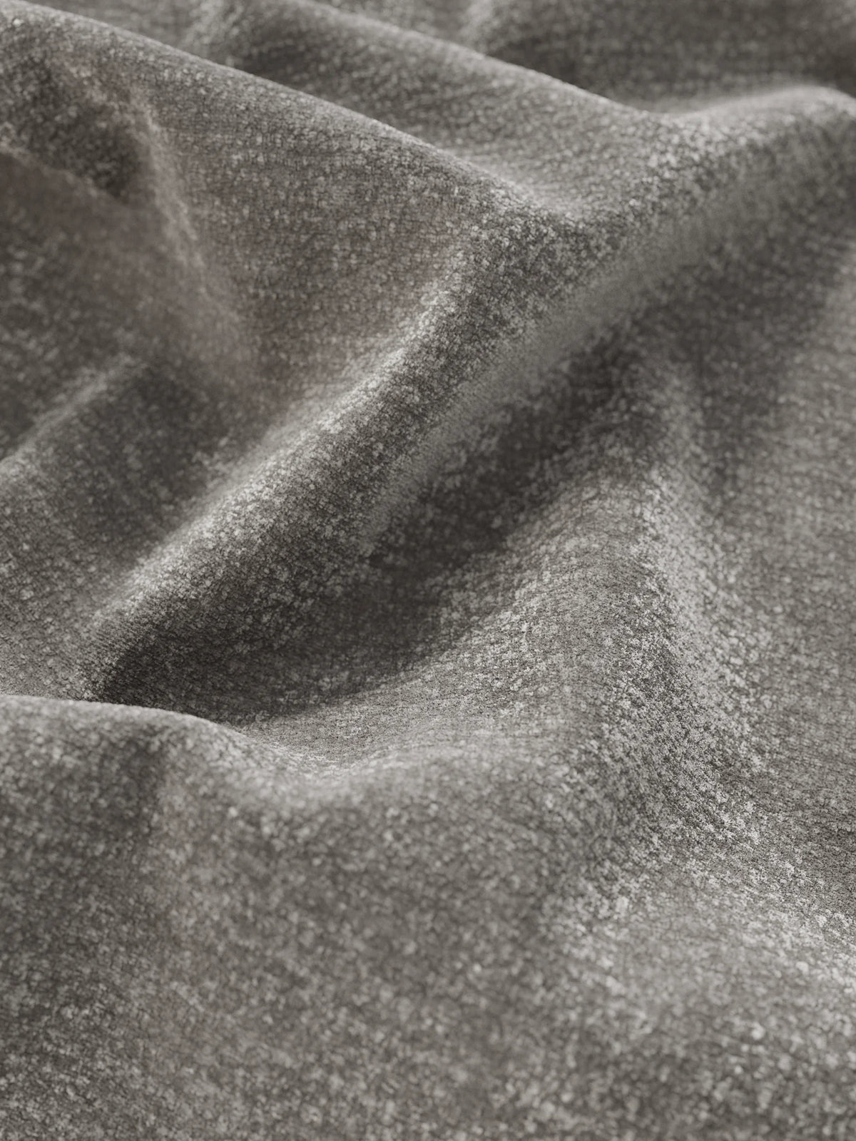Primo piano di un tessuto color grigio antracite dall’effetto vellutato con una delicata lucentezza, drappeggiato in morbide pieghe ondulate su un letto imbottito ONYX con vano contenitore e testiera verticale in tessuto certificato Oeko-Tex®.