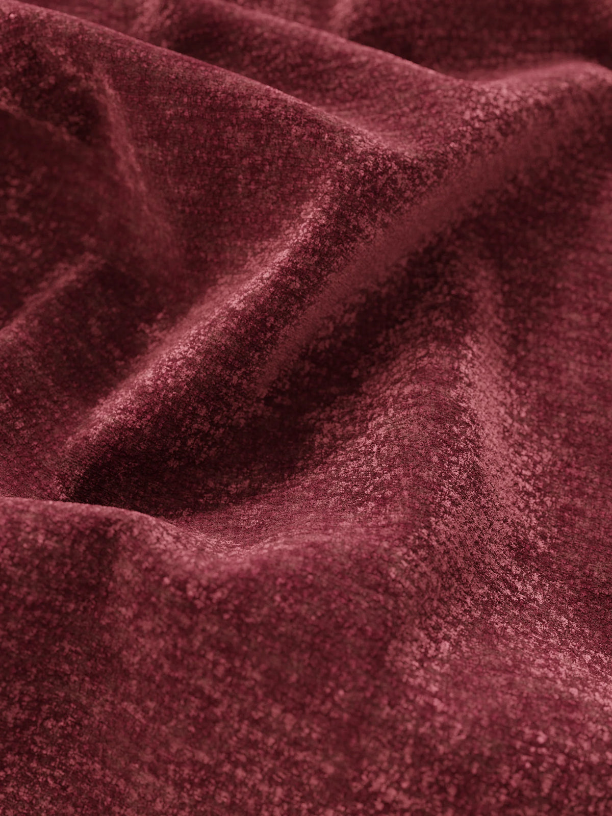 Primo piano su un tessuto in velluto color bordeaux intenso che riveste il letto imbottito ARKAM, caratterizzato da morbide pieghe che creano sottili giochi di luci e ombre sulla superficie ricca e strutturata della testiera imbottita.