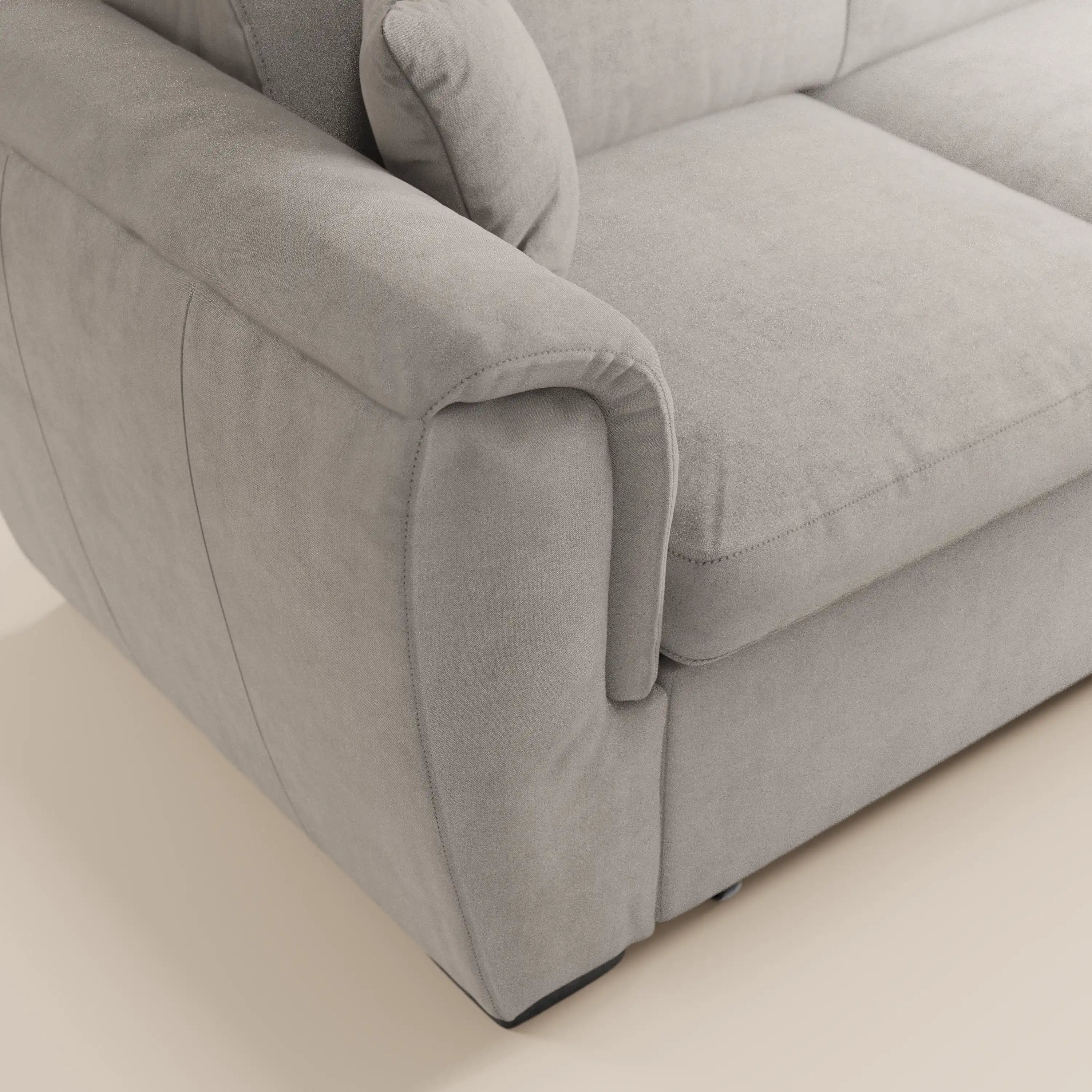Primo piano del divano angolare reversibile Titano di Divani.Store, caratterizzato da un tessuto Oeko-Tex® lavabile di colore grigio chiaro, poggiatesta reclinabili, cuscino di seduta spesso, pouf contenitore e un design moderno e minimalista. L'attenzione è concentrata sul bracciolo sinistro e sul cuscino.