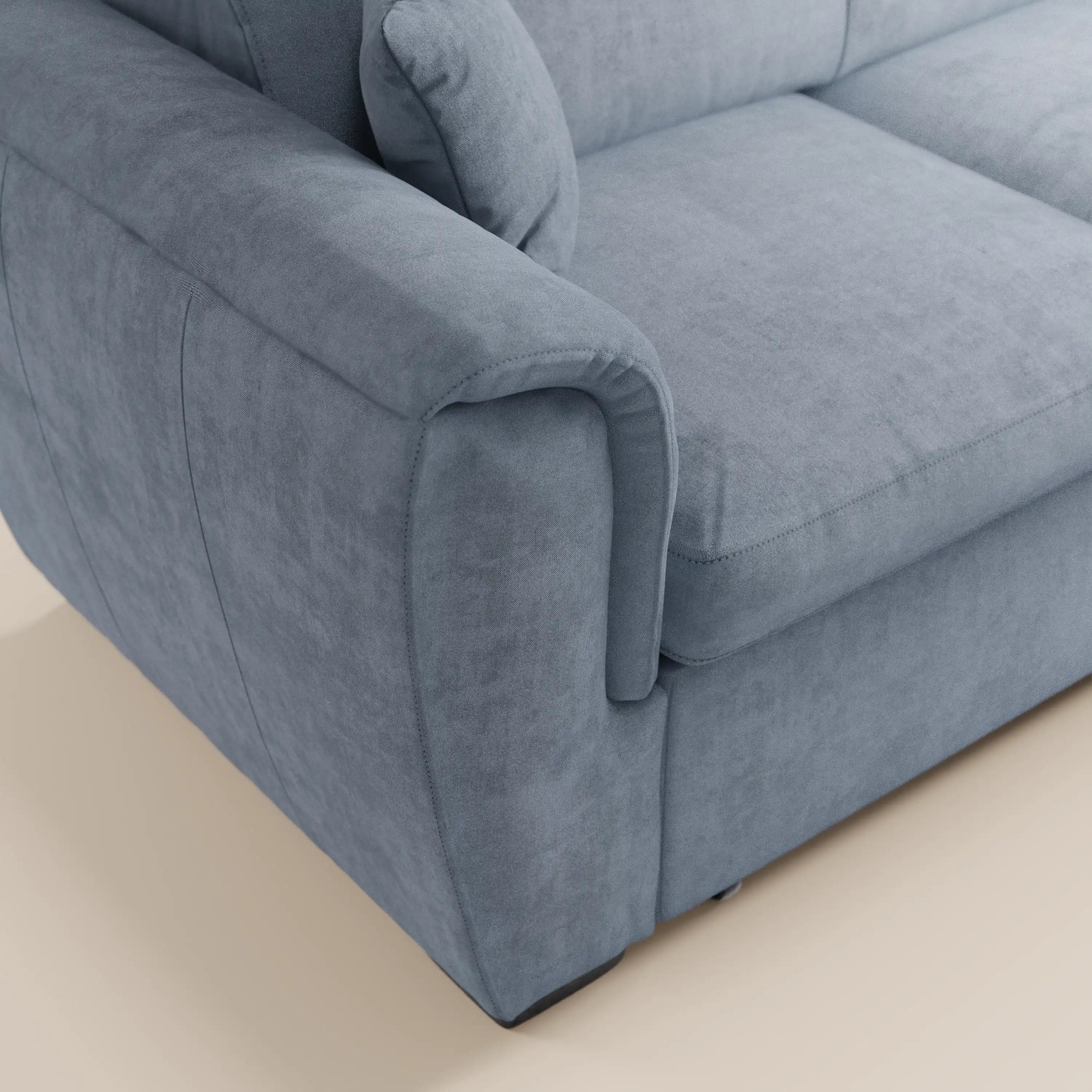 Primo piano del divano angolare reversibile con letto estraibile e pouf contenitore Titano di Divani.Store, rivestito in morbido tessuto Smacchiabile Oeko-Tex® di colore azzurro chiaro. L’immagine mette in risalto il bracciolo, la seduta e un cuscino dello schienale dalla trama morbida e dalle cuciture precise. I poggiatesta reclinabili aggiungono comfort, mentre il divano poggia su un pavimento di colore chiaro.