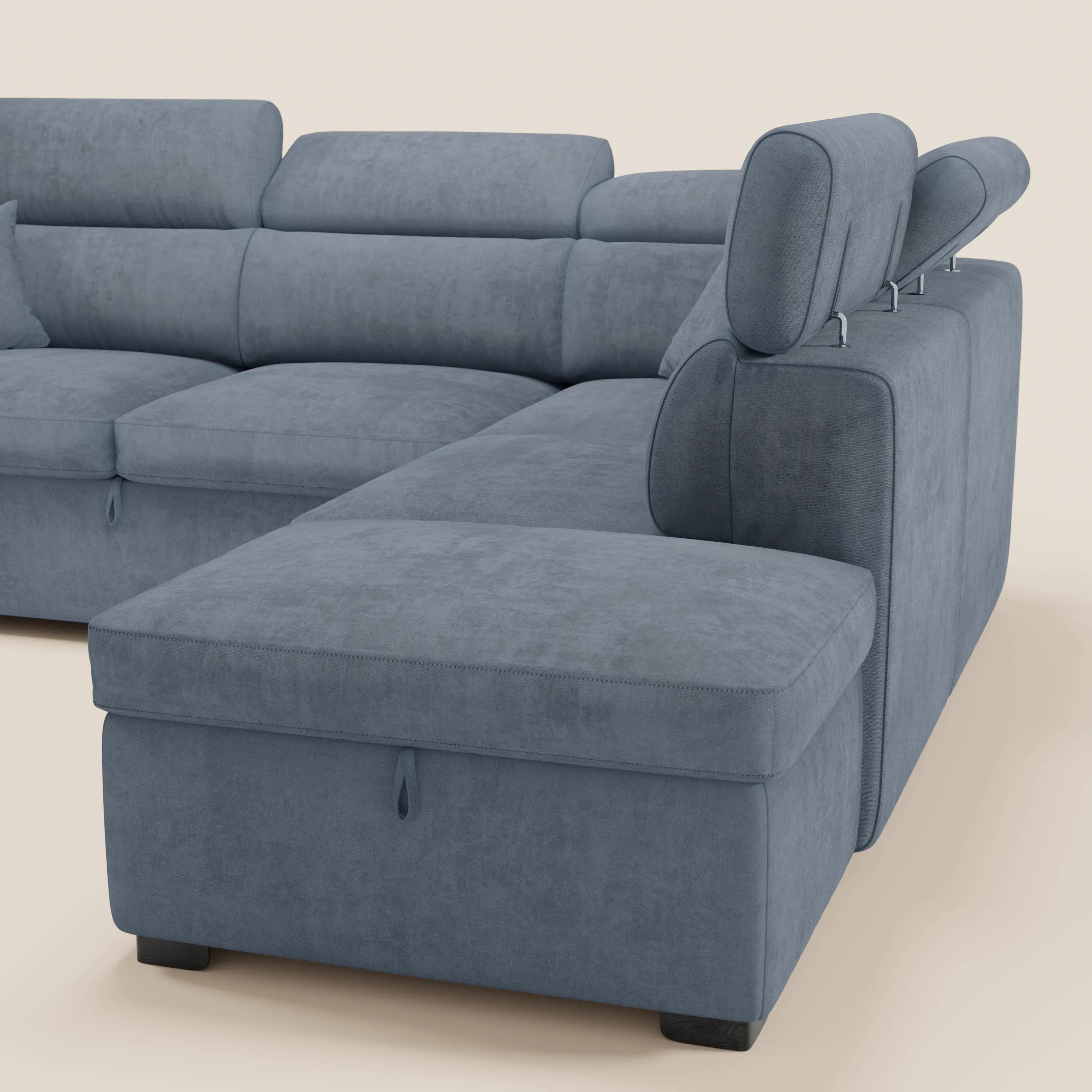 Un moderno divano angolare reversibile Titano con letto estraibile e pouf contenitore di Divani.Store, rivestito in morbido tessuto blu antimacchia certificato Oeko-Tex®, poggia su un pavimento beige chiaro. È dotato di poggiatesta reclinabili, schienale basso, sedute ampie e una sezione chaise longue. Questo divano componibile vanta un design elegante e minimalista con gambe corte nere.