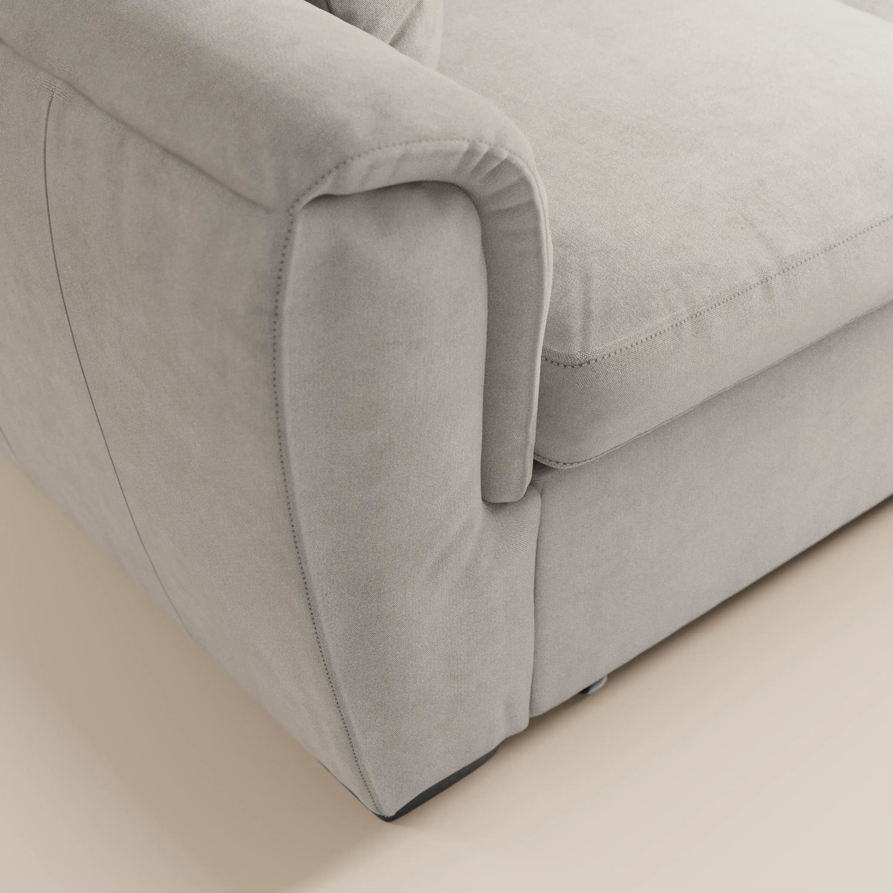 Primo piano sul bracciolo e sulla seduta del divano a 2 posti estraibile Titano di Divani.Store, realizzato in morbido tessuto simile alla pelle scamosciata, certificato Oeko-Tex® e resistente alle macchie, con cuciture a vista e imbottitura soffice. Sfondo: pavimento liscio di colore chiaro.