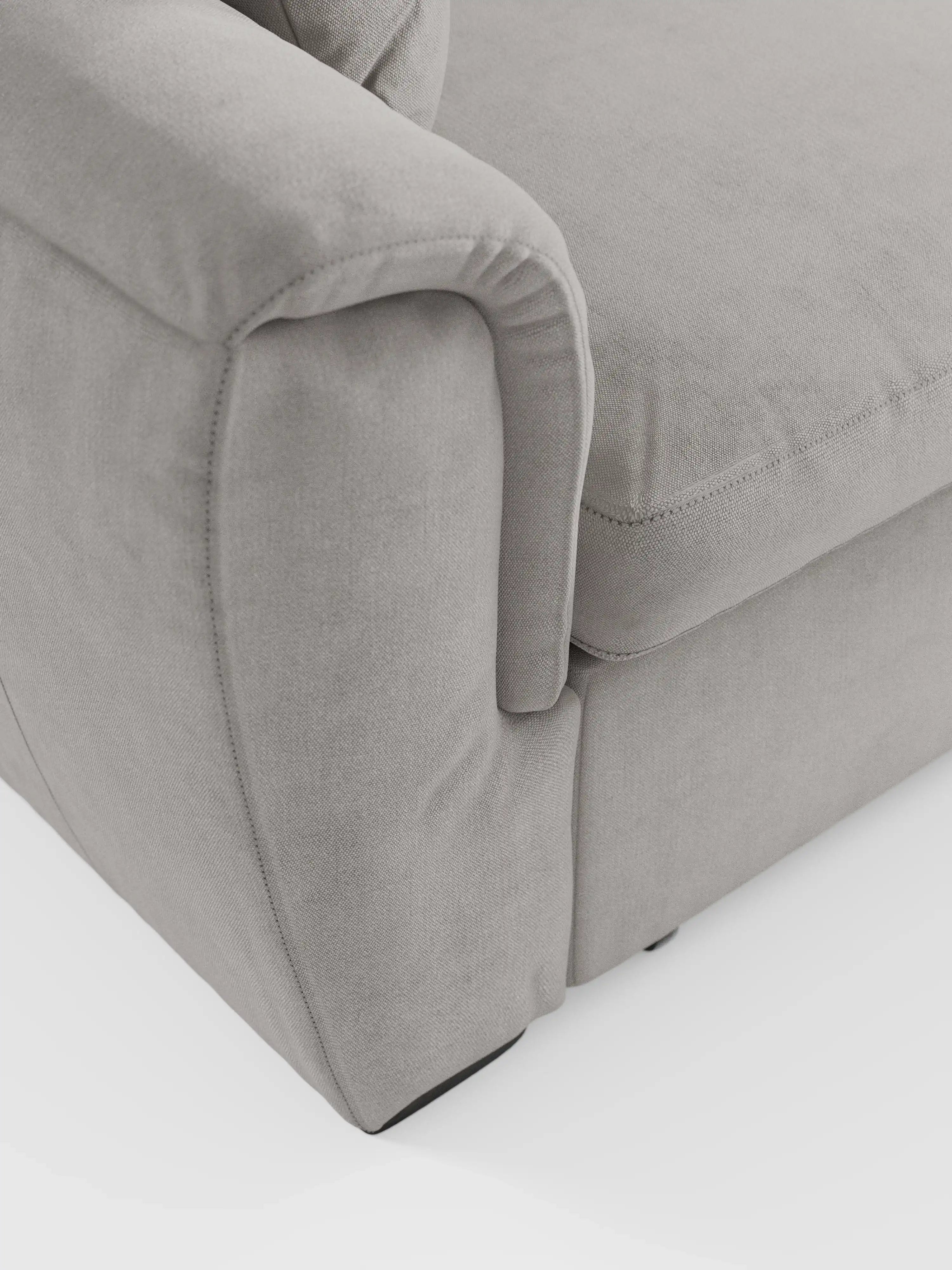 Primo piano del divano letto Titano con penisola reversibile, contenitore, poggiatesta reclinabili ed elemento estraibile in tessuto smacchiabile di Divani.Store. Il divano imbottito grigio chiaro presenta un tessuto morbido, liscio e facile da pulire, con cuciture a vista. L'immagine mette in risalto i braccioli curvi e il cuscino della seduta su uno sfondo bianco.