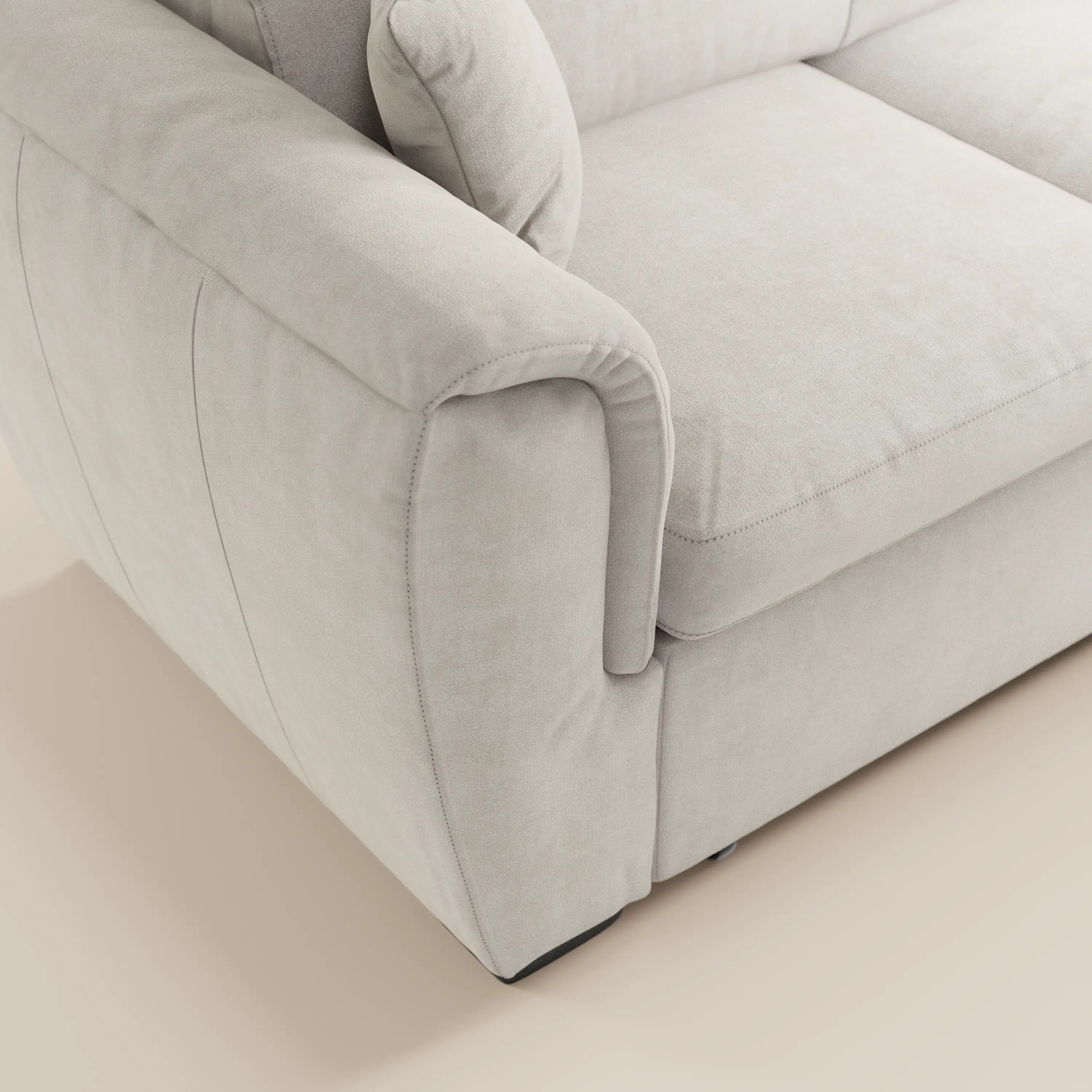 Primo piano del bracciolo sinistro e della seduta del divano letto Titano con penisola reversibile di Divani.Store, in grigio chiaro, caratterizzato da un morbido tessuto antimacchia, cuciture discrete, ampio bracciolo arrotondato e base beige.