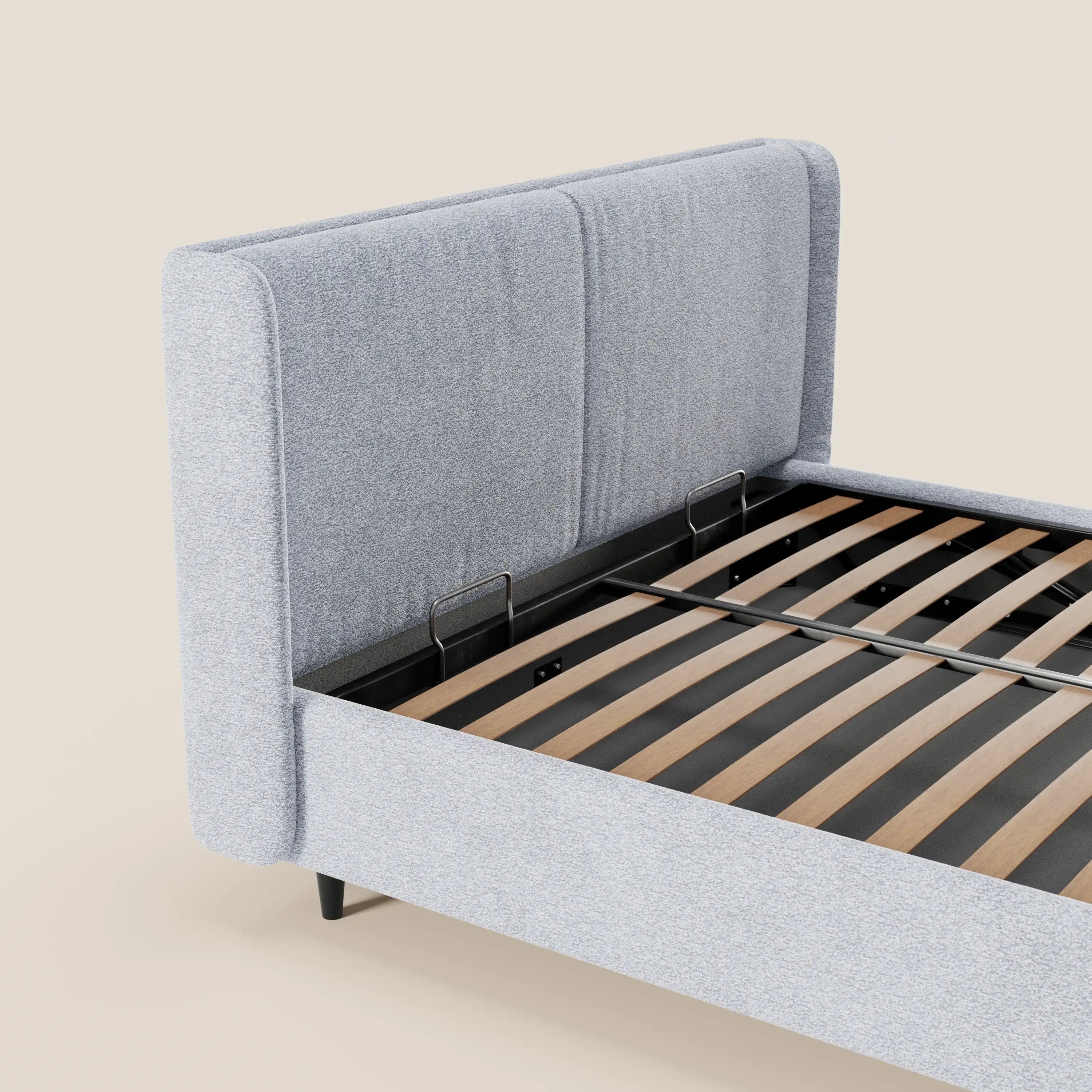 Il letto di design VALKIRIA di Letti.store presenta una testiera avvolgente rivestita in tessuto grigio chiaro certificato Oeko-Tex®, con 2 cuscini imbottiti, doghe in legno a vista, base in metallo nero e gambe corte nere, il tutto su uno sfondo beige con vano contenitore.