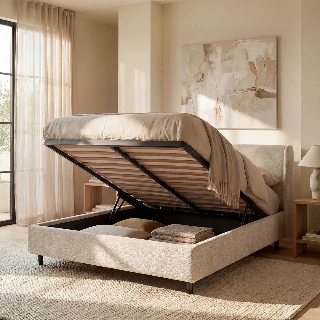 Il letto di design VALKIRIA di Letti.store è caratterizzato da un tessuto beige certificato Oeko-Tex®, una testiera avvolgente con 2 cuscini imbottiti e un materasso sollevabile che rivela un ampio vano contenitore sotto il letto per cuscini e biancheria da letto. La camera è illuminata da una luce soffusa, con tende trasparenti e comodini in legno.
