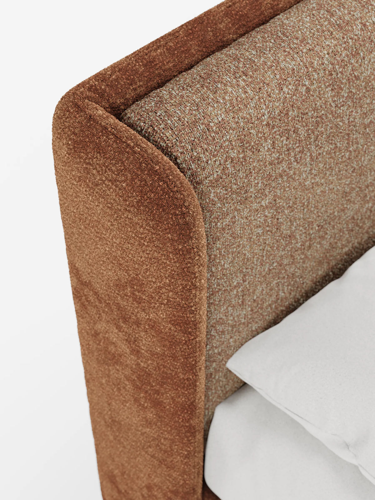 Un primo piano di un letto imbottito VALKIRIA bicolore con contenitore, dalle linee curve: cuscini dello schienale e testiera curva avvolgente, con un pannello laterale marrone scuro, una superficie interna beige screziata e un cuscino bianco.