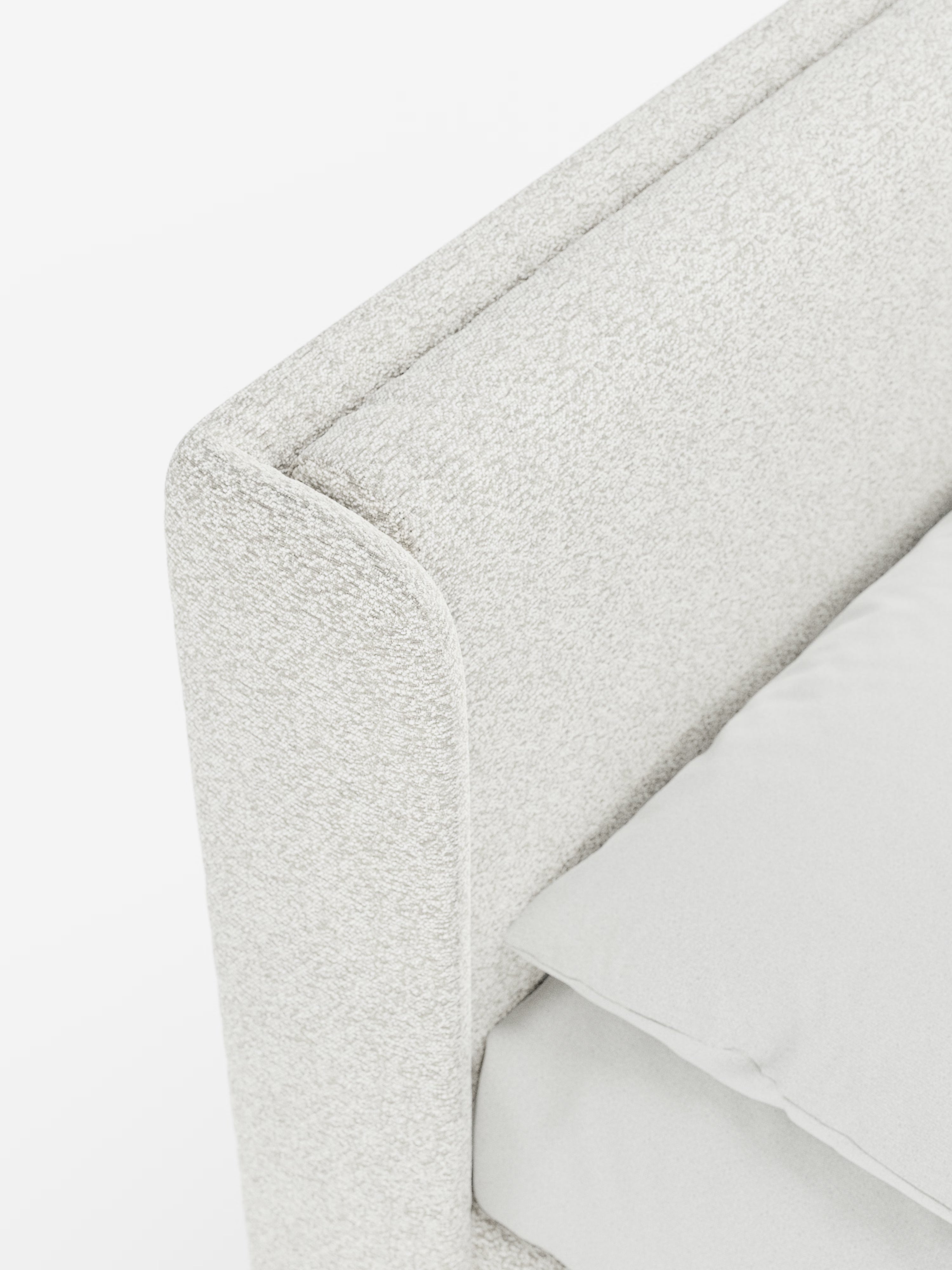 Primo piano del letto di design VALKIRIA con contenitore e testiera avvolgente di Letti.store, caratterizzato da un tessuto Oeko-Tex® dalla trama leggera e da bordi morbidi e arrotondati della testiera, con due soffici cuscini imbottiti. Sul materasso sono parzialmente visibili un cuscino bianco e un lenzuolo disposti con cura, che mettono in risalto il design contemporaneo di questo elegante letto imbottito su uno sfondo luminoso e minimalista.