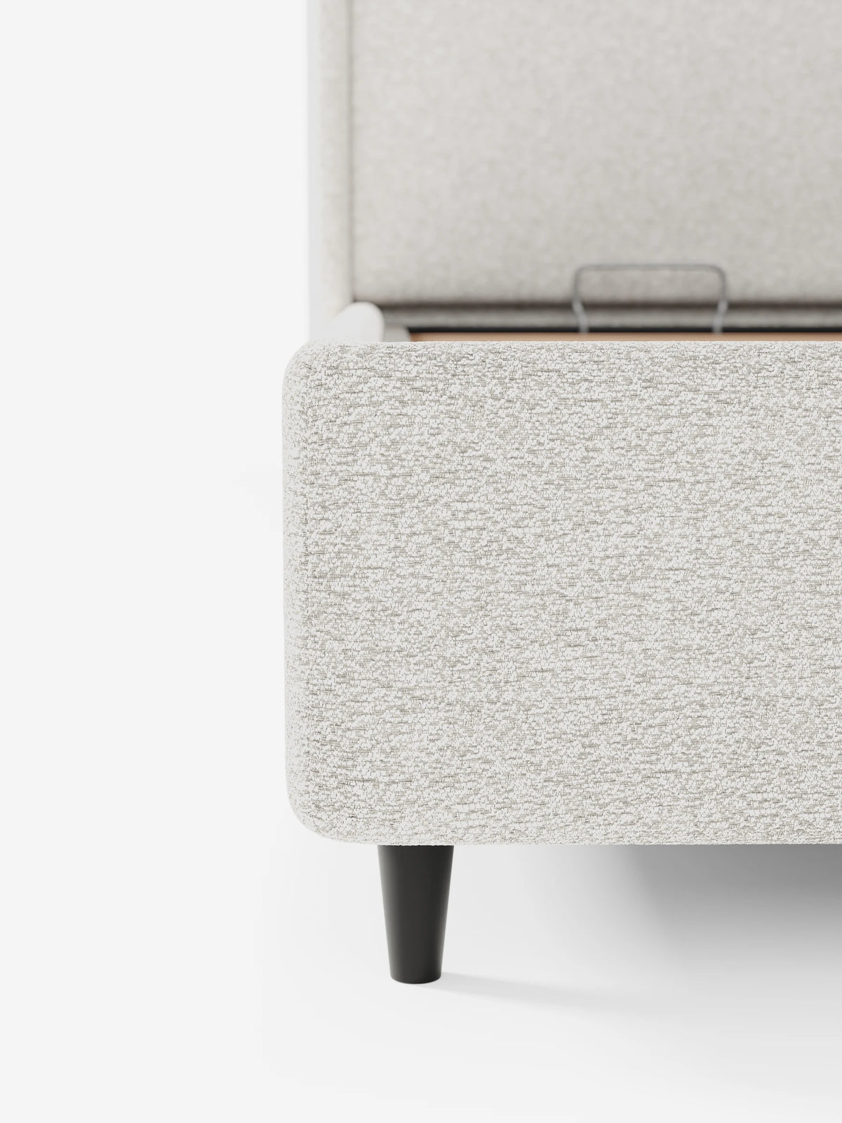 Un primo piano del letto di design VALKIRIA con vano contenitore e testiera avvolgente, rivestito in tessuto beige testurizzato, con una gamba affusolata scura e un vano contenitore rialzato dotato di una maniglia di sollevamento in metallo.