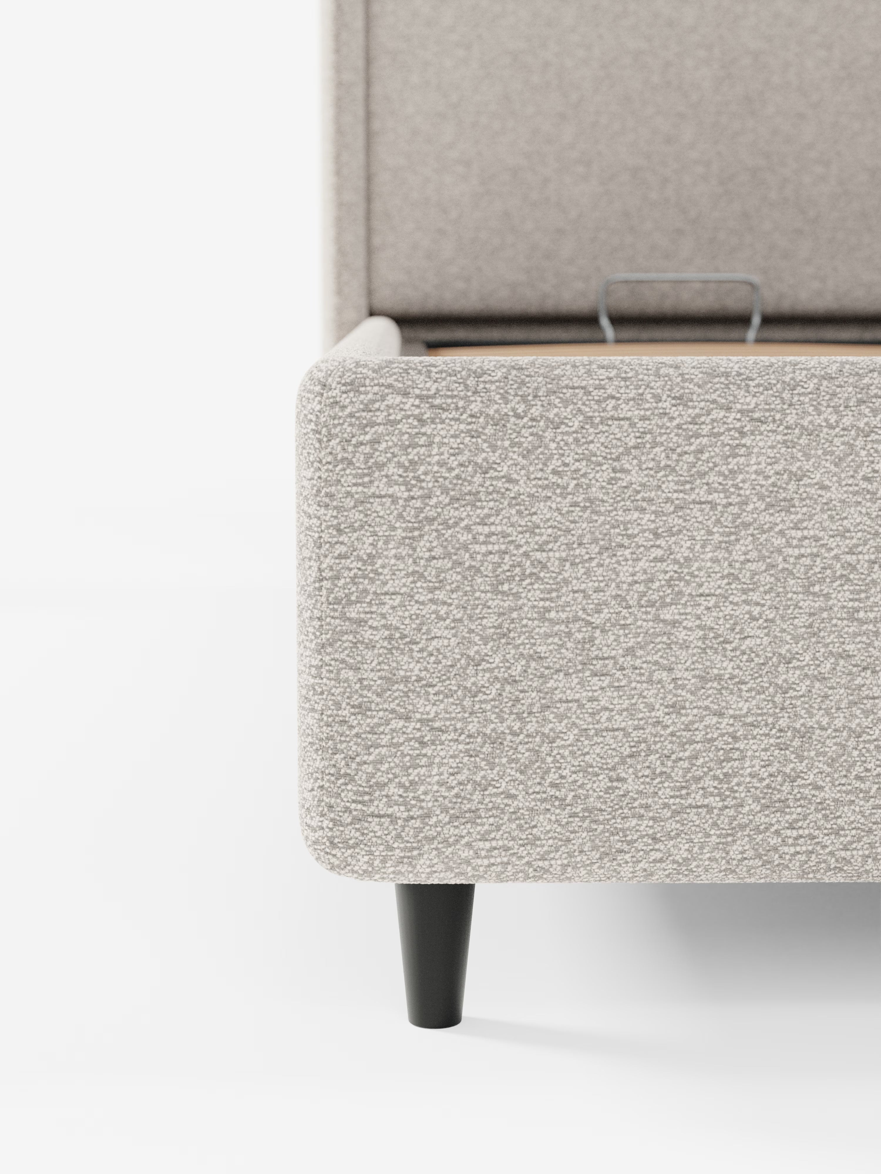 Primo piano dell'angolo del letto di design VALKIRIA di Letti.store, realizzato in tessuto grigio chiaro certificato Oeko-Tex®, che mette in risalto la struttura imbottita con texture e la gamba affusolata in legno nero, su sfondo bianco. Sono visibili parte della testiera avvolgente con due cuscini imbottiti e la rete a doghe interna con vano contenitore, che ne sottolineano il design contemporaneo.