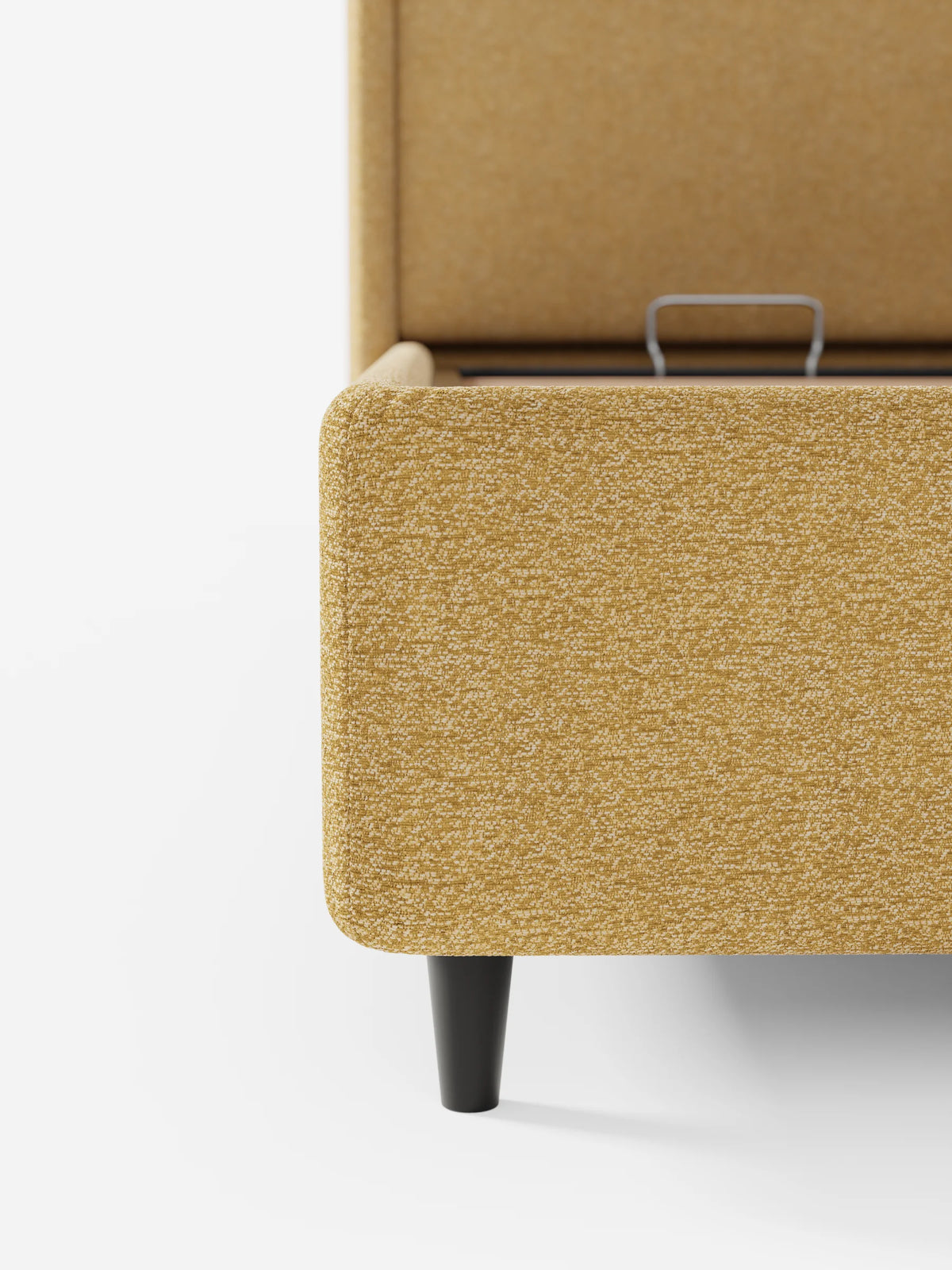 Un primo piano di un letto di design VALKIRIA color senape con vano contenitore e testiera avvolgente, caratterizzato da una base rialzata, tessuto testurizzato e gambe nere affusolate su uno sfondo bianco pulito.