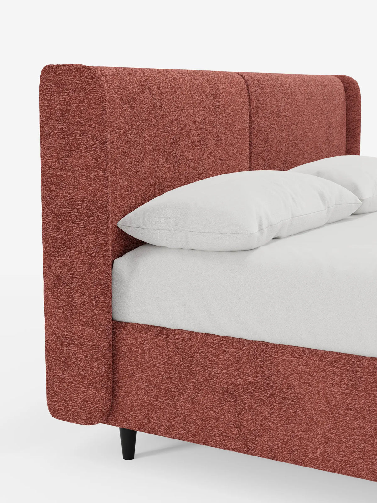 Il letto di design VALKIRIA con contenitore e testiera avvolgente è una struttura imbottita di colore rosso terracotta, caratterizzata da un’alta testiera avvolgente, due cuscini bianchi su biancheria da letto bianca e corte gambe cilindriche nere che si stagliano contro una parete bianca.