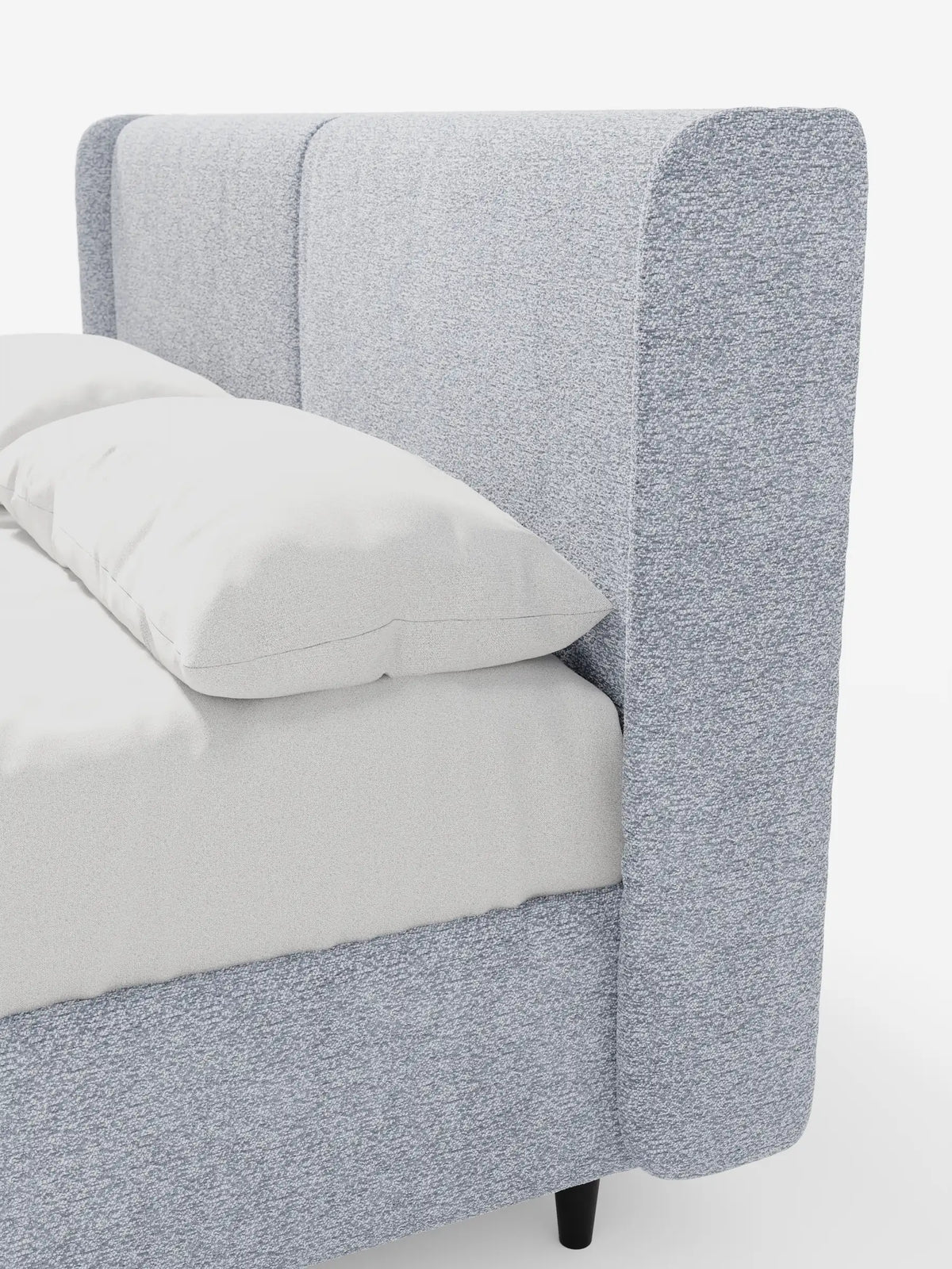 Una vista laterale del letto di design VALKIRIA con contenitore e testiera avvolgente, caratterizzato da un’alta testiera imbottita di colore azzurro, due morbidi cuscini bianchi su un lenzuolo grigio chiaro e piccoli piedini scuri su uno sfondo bianco.
