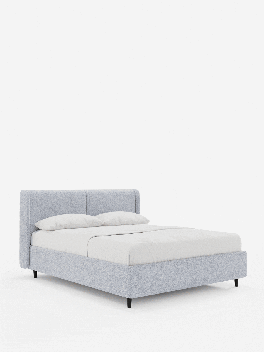 Un letto di design VALKIRIA grigio chiaro con contenitore e testiera avvolgente, caratterizzato da una testiera curva e avvolgente, morbidi cuscini, biancheria da letto bianca e gambe corte, scure e affusolate, su uno sfondo bianco a tinta unita.