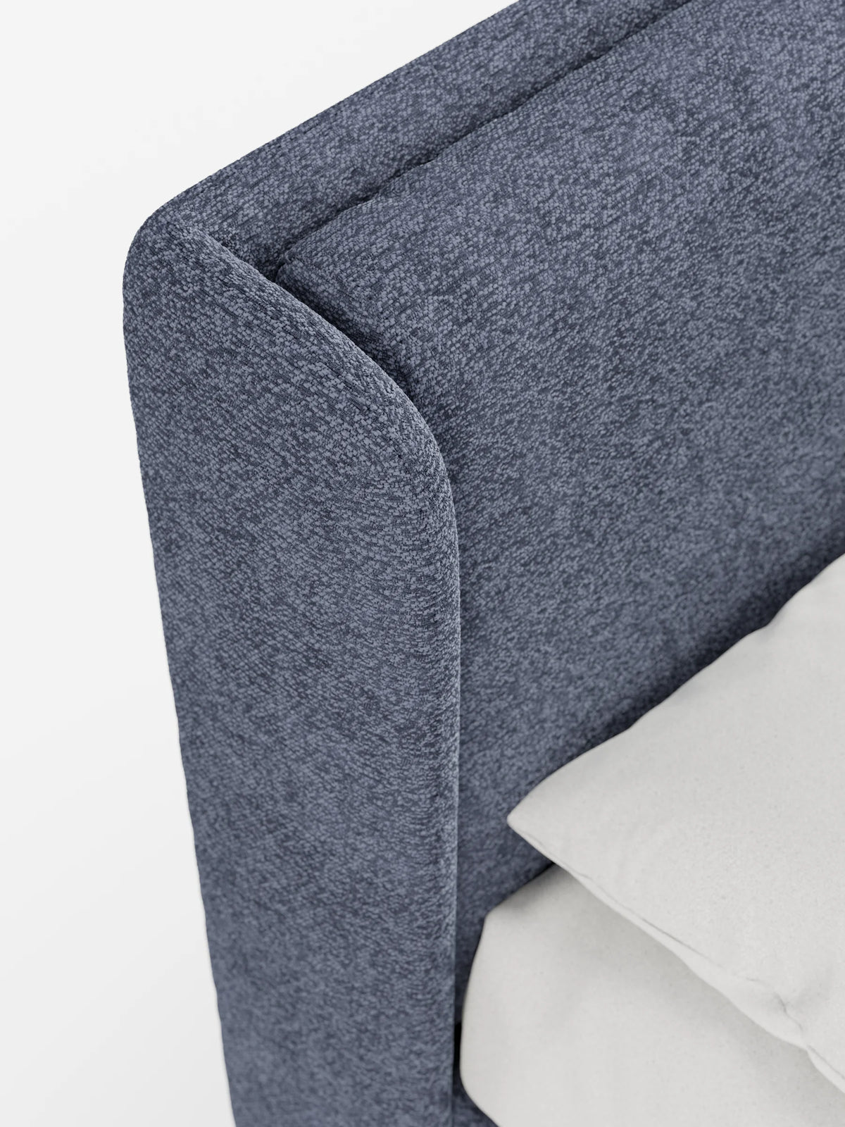 Un primo piano di un letto di design VALKIRIA blu scuro con finitura testurizzata, dotato di vano contenitore e testiera avvolgente con fianchi curvi, con un cuscino di colore chiaro appoggiato alla testiera, su uno sfondo bianco a tinta unita.