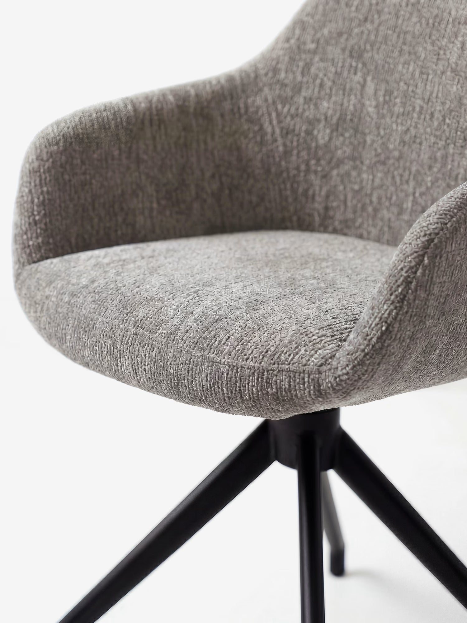 Un primo piano della sedia imbottita Vico di Divani.Store, caratterizzata da un morbido tessuto soft-touch certificato OEKO-TEX®, braccioli ricurvi e gambe in metallo nero. Lo sfondo bianco a tinta unita ne esalta il design raffinato e il comfort.