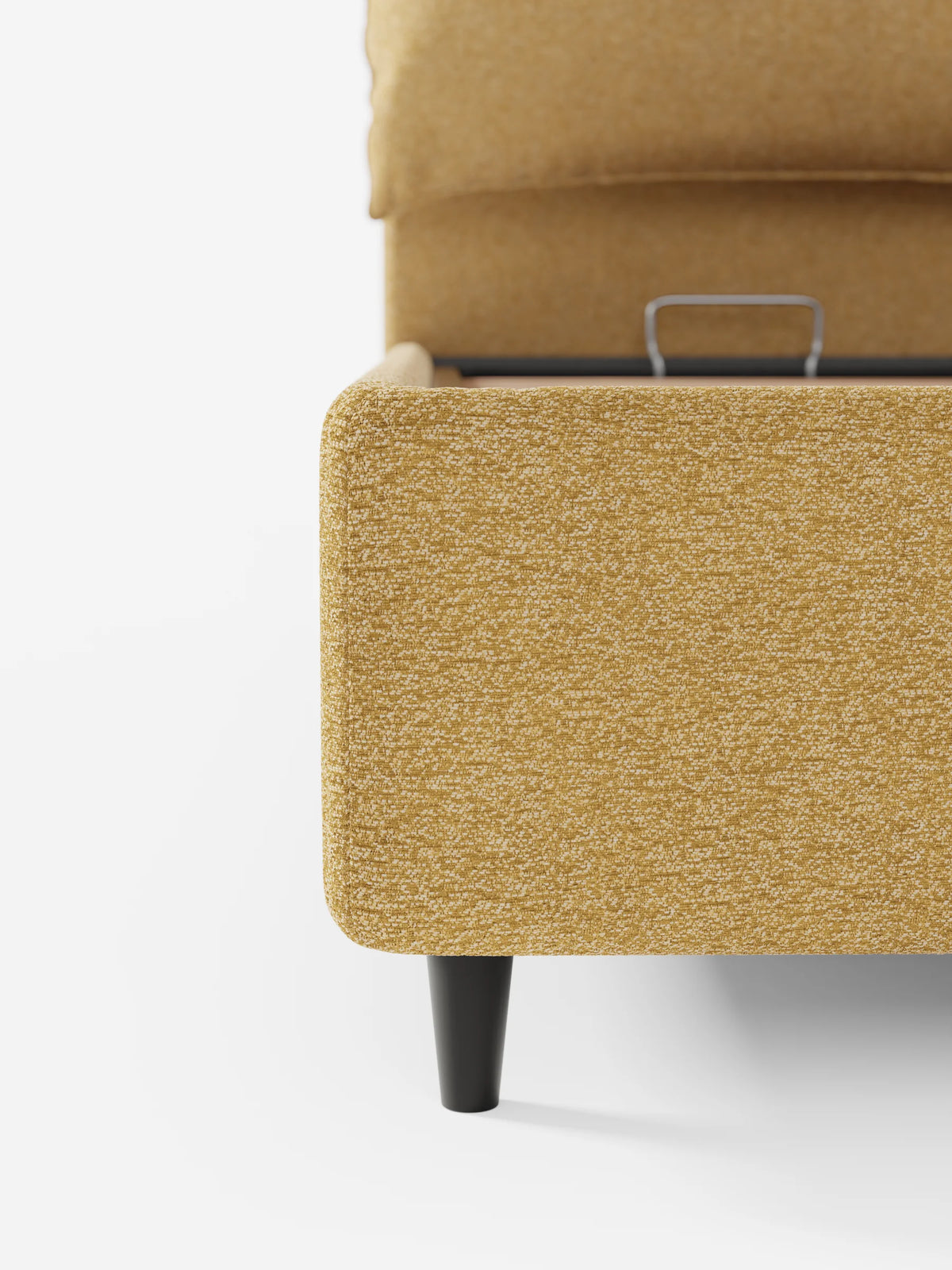 Un primo piano di un divano letto ZAYRON color giallo senape, imbottito, con vano contenitore e morbidi cuscini regolabili, che mostra il vano contenitore parzialmente aperto, il tessuto a trama, le gambe affusolate scure e una maniglia argentata su sfondo bianco.