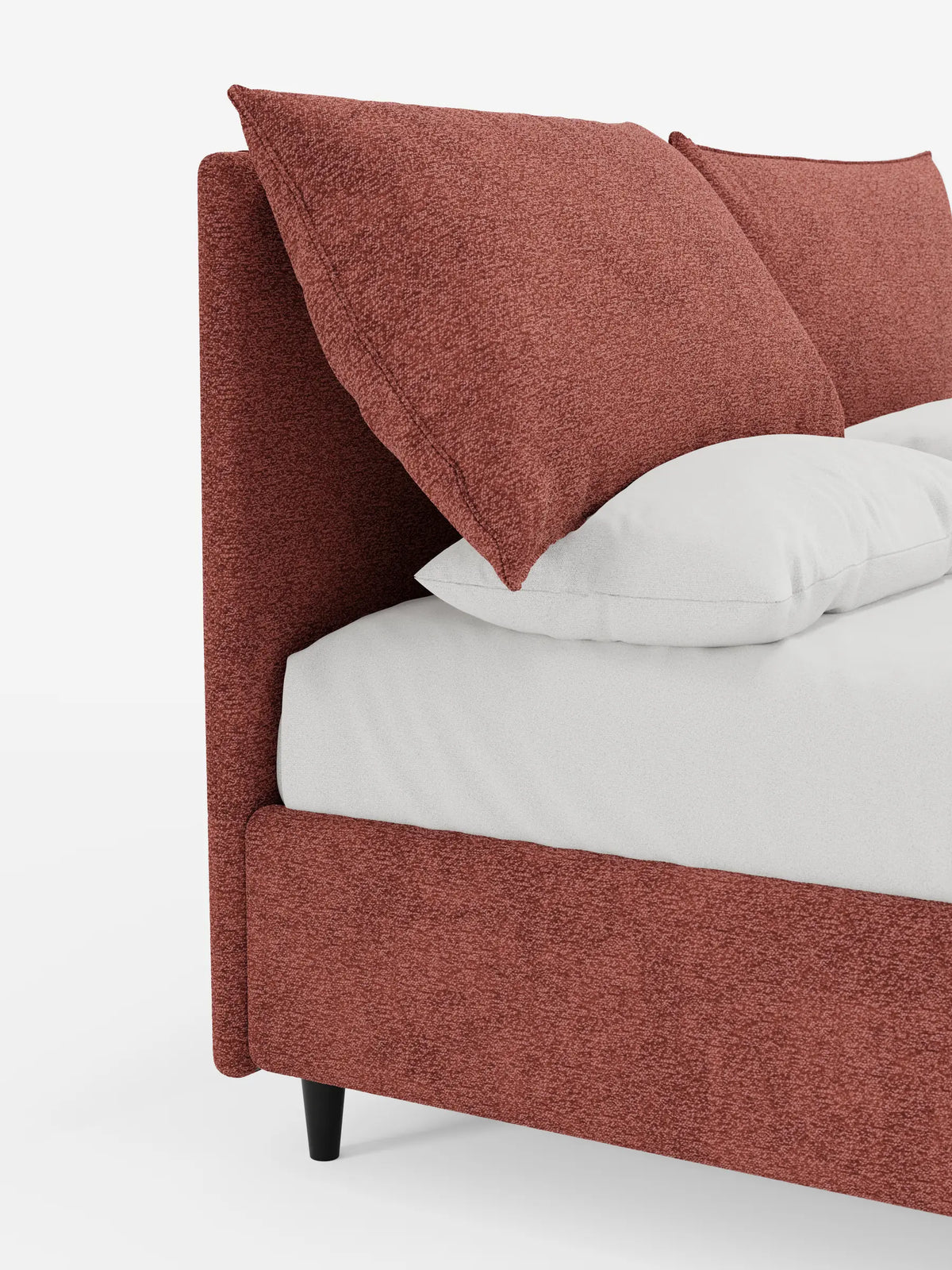 Un primo piano di un letto ZAYRON color ruggine, imbottito, con contenitore e morbidi cuscini regolabili, con grandi cuscini morbidi, lenzuola bianche a tinta unita e una slanciata gamba nera che sostiene la base.