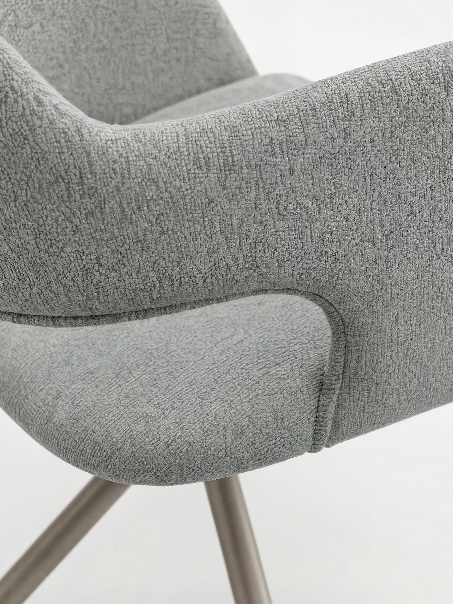 Primo piano di Zefira, la moderna poltrona imbottita di Divani.Store, caratterizzata da un tessuto grigio chiaro effetto cotone, seduta e schienale imbottiti e sagomati con braccioli, e una base in metallo color champagne. Sfondo bianco a tinta unita.