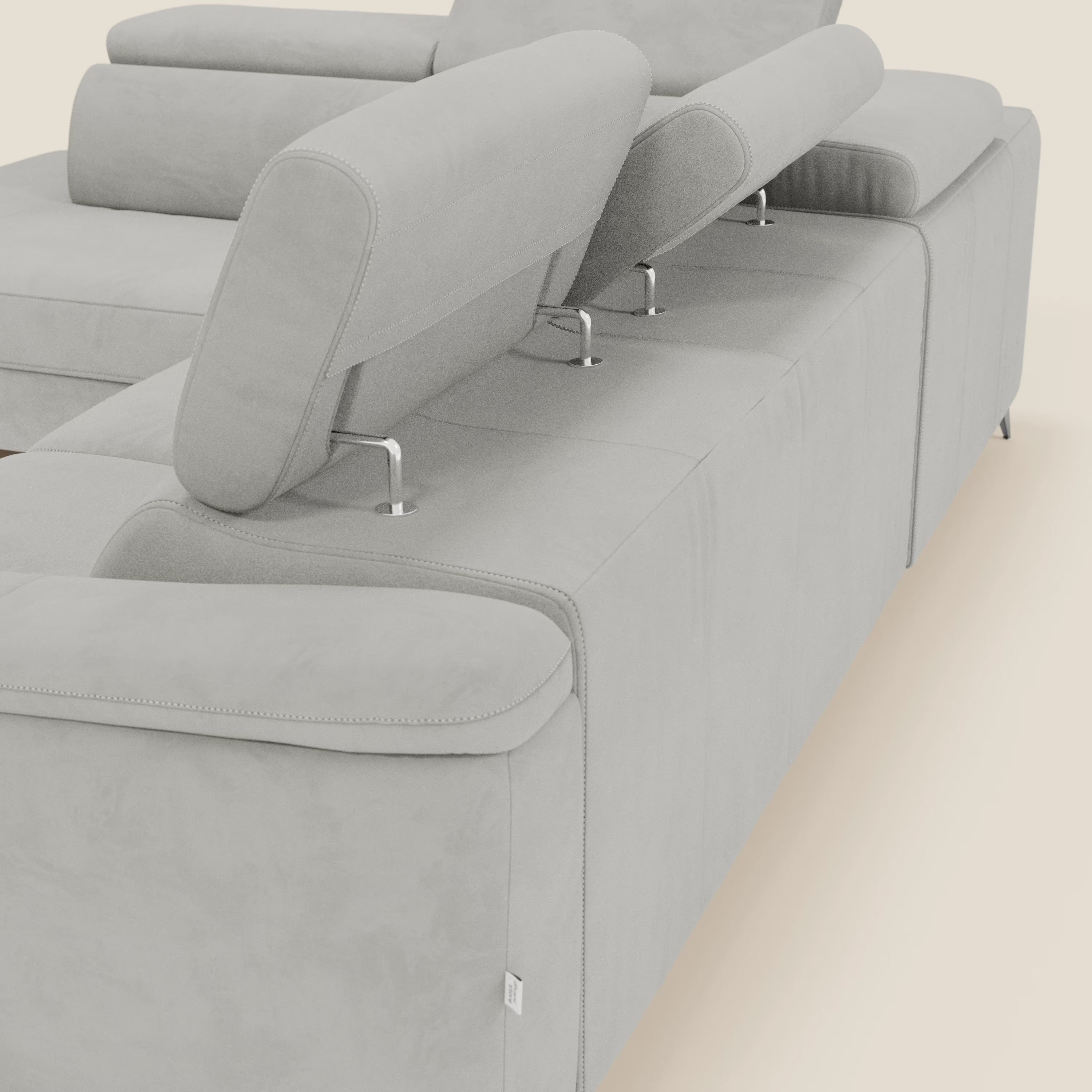 Primo piano di Arcos Divano angolare di Divani.Store, caratterizzato da gambe alte, poggiatesta regolabili, rivestimento in microfibra impermeabile grigio chiaro T11 con cuciture a vista e chaise longue estraibile su sfondo tinta unita.
