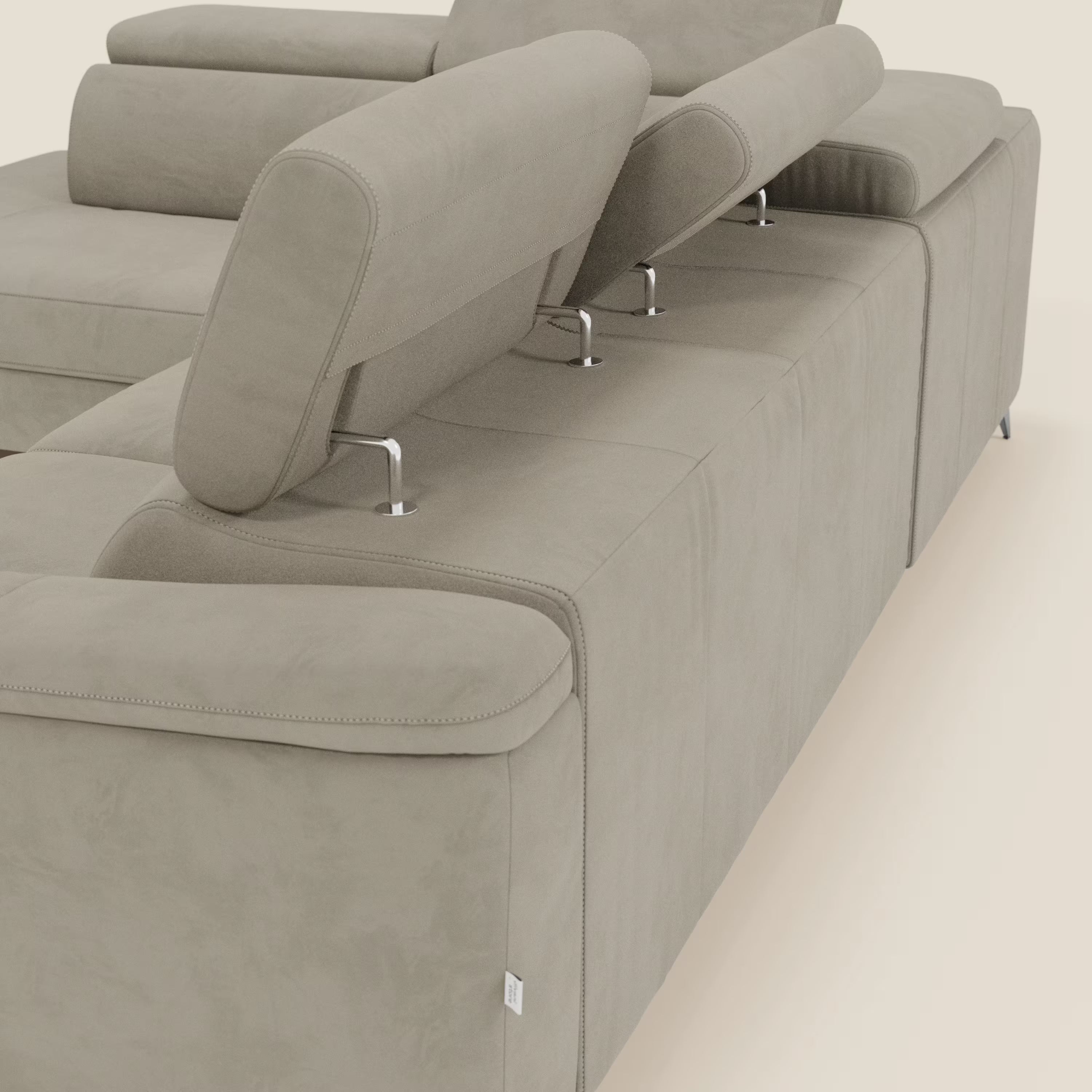 Un primo piano del divano angolare Arcos di Divani.Store in microfibra impermeabile T11 tortora, che mette in evidenza le gambe alte, gli ampi braccioli e i poggiatesta regolabili per il massimo comfort. Il design moderno è caratterizzato da linee pulite e da una chaise longue estraibile.