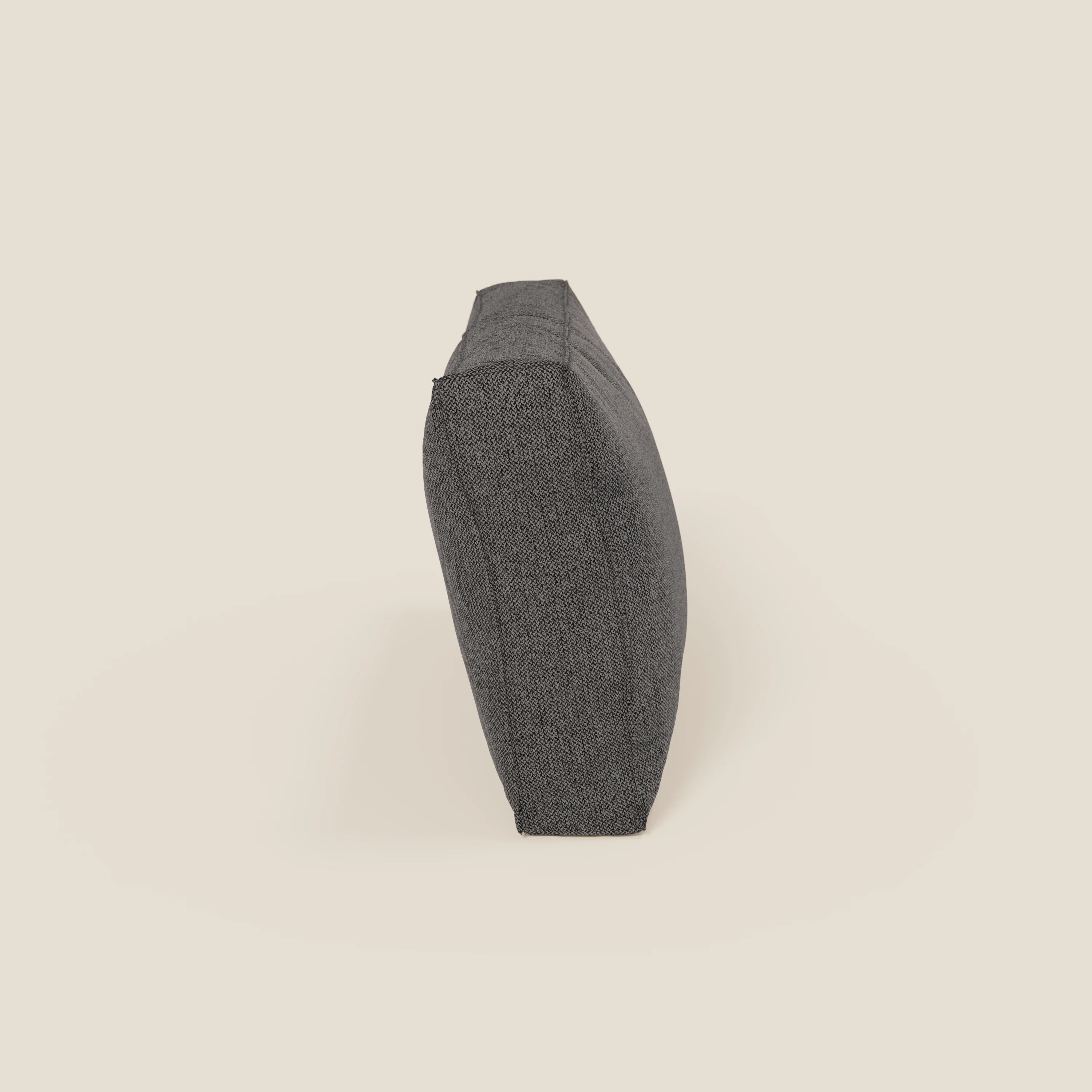 Il cuscino schienale BonBon di Divani.Store, in tessuto smacchiabile T23 antracite e disponibile in 2 misure, si poggia sul bordo sottile davanti a uno sfondo beige chiaro-linee pulite e ideali per il divano modulare BonBon.