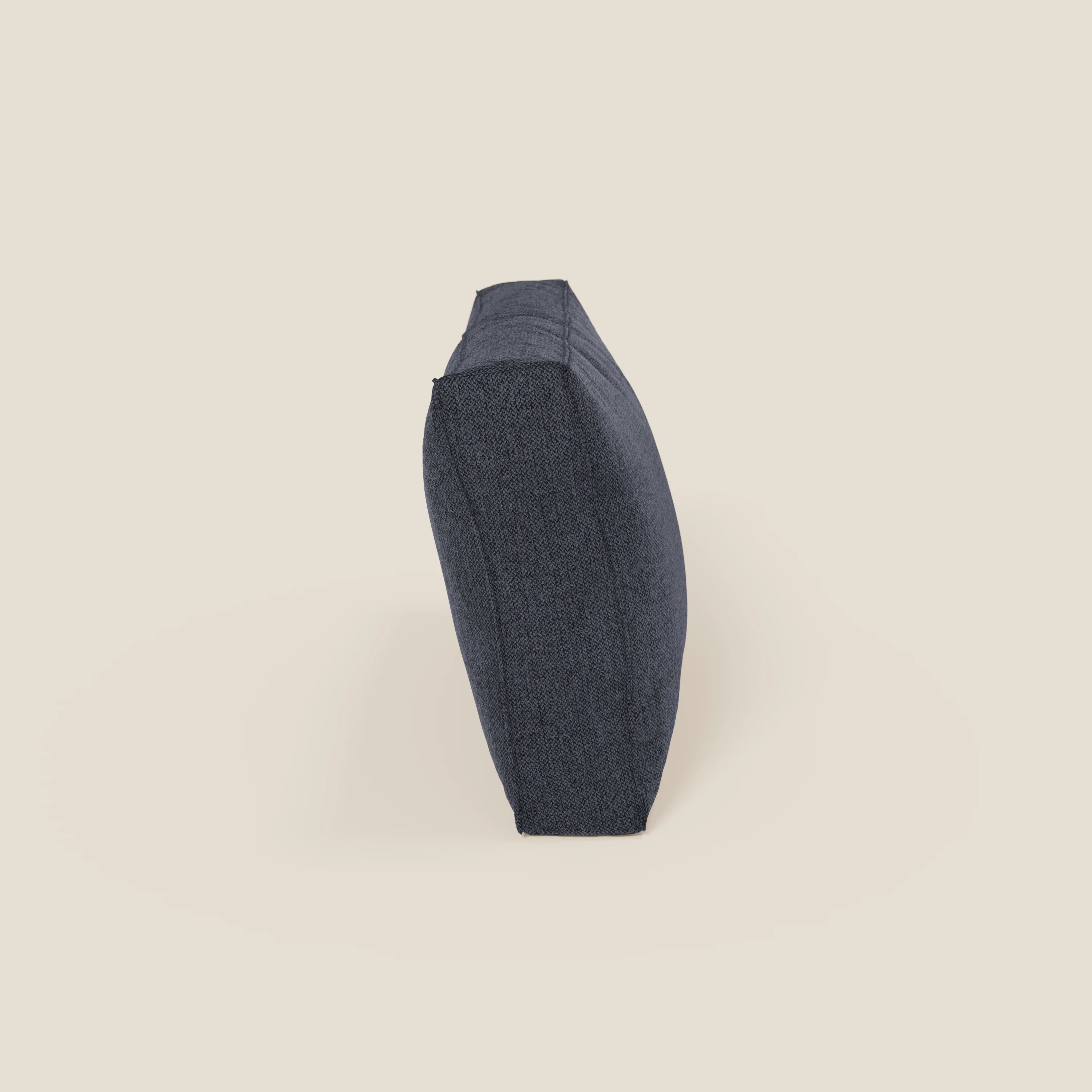Un cuscino schienale BonBon di Divani.Store in tessuto antimacchia T23 blu ardesia si erge sul bordo stretto su uno sfondo beige chiaro, mettendo in evidenza la sua forma rettangolare e la sottile trama. Disponibile in due misure.