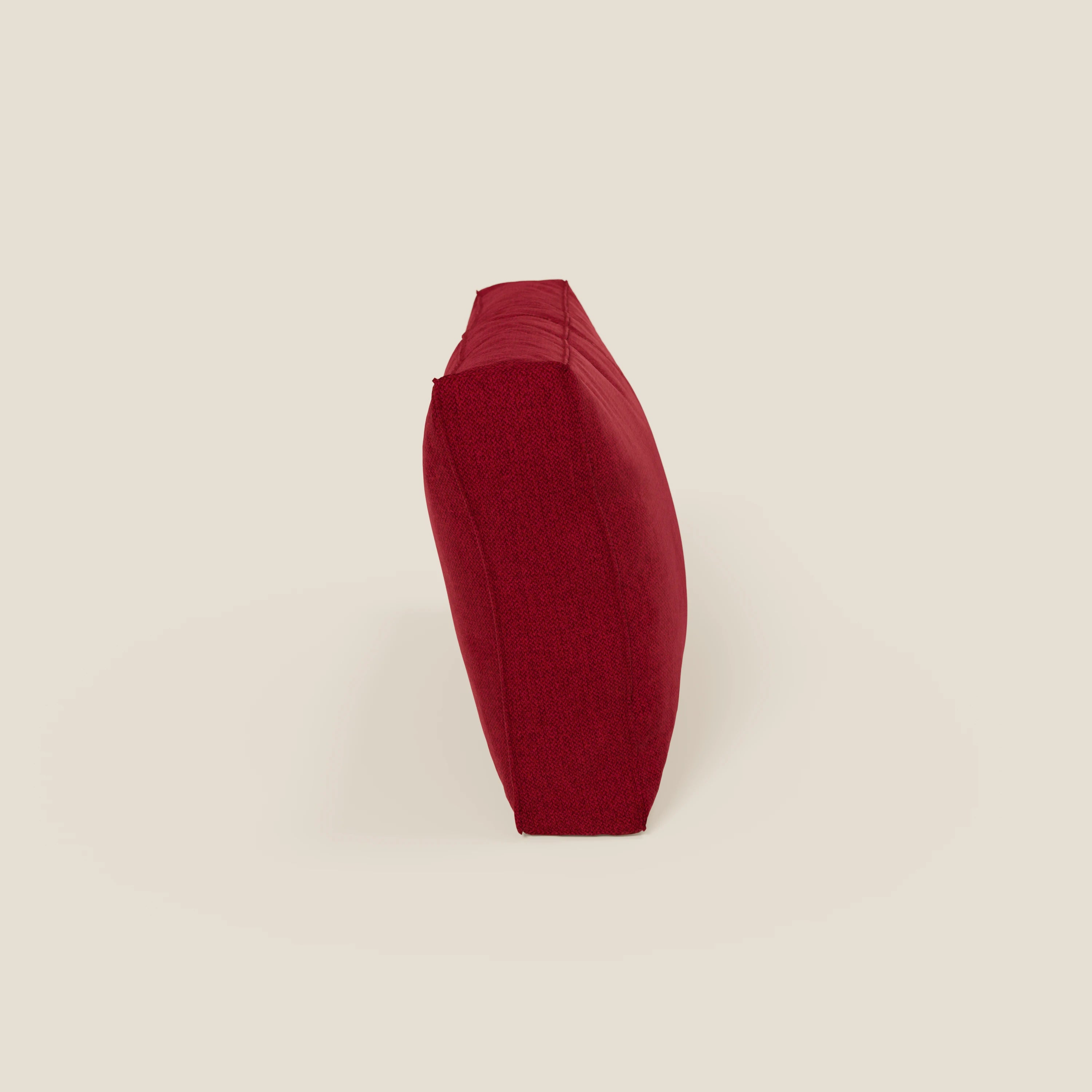 Il cuscino schienale BonBon di Divani.Store, presentato in tessuto antimacchia T23 bordeaux, si erge sul fianco su uno sfondo beige chiaro. La sua forma rettangolare e massiccia e la sua consistenza sono visibili lateralmente. Disponibile in 2 misure.