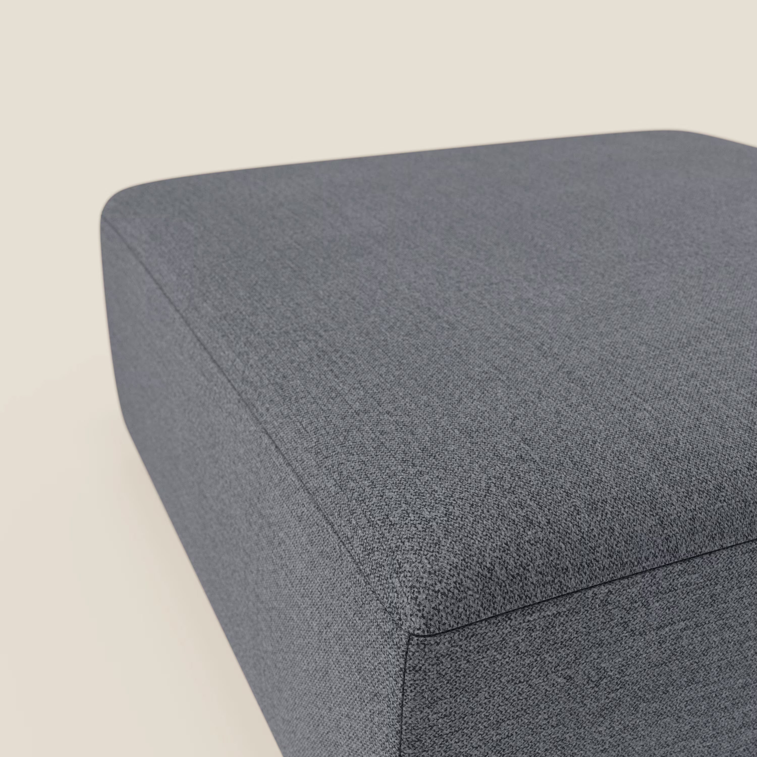 Un primo piano del pouf divano modulare BonBon di Divani.Store, presentato in tessuto antimacchia T23 blu grafite, ne evidenzia le linee pulite e la consistenza morbida su uno sfondo bianco sporco, concentrandosi sull'angolo superiore e laterale.