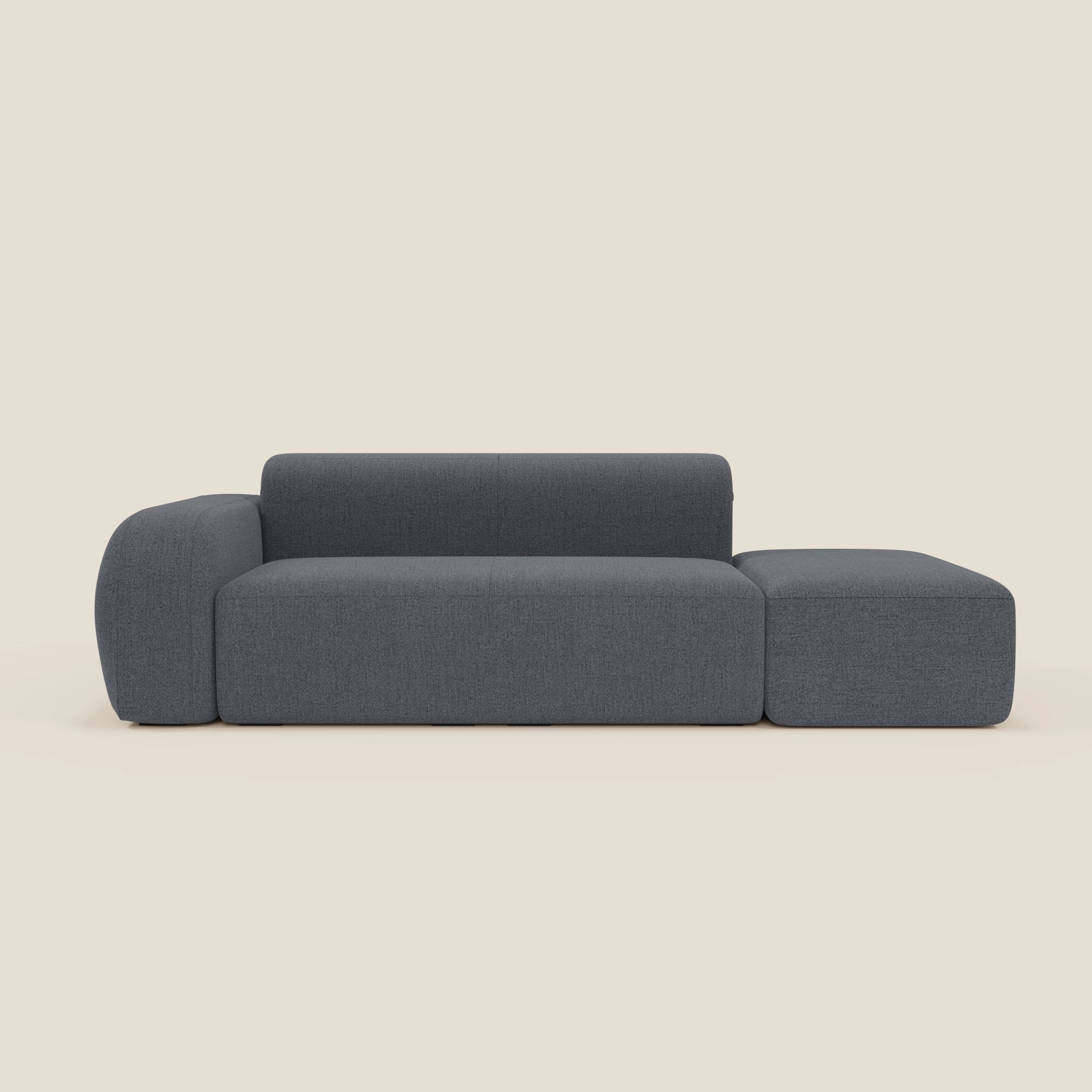 Il BonBon Divano componibile di Divani.Store è caratterizzato da un tessuto antimacchia T23 blu grafite, un bracciolo sinistro, una chaise longue destra allungata e un pouf terminale, su uno sfondo bianco sporco.