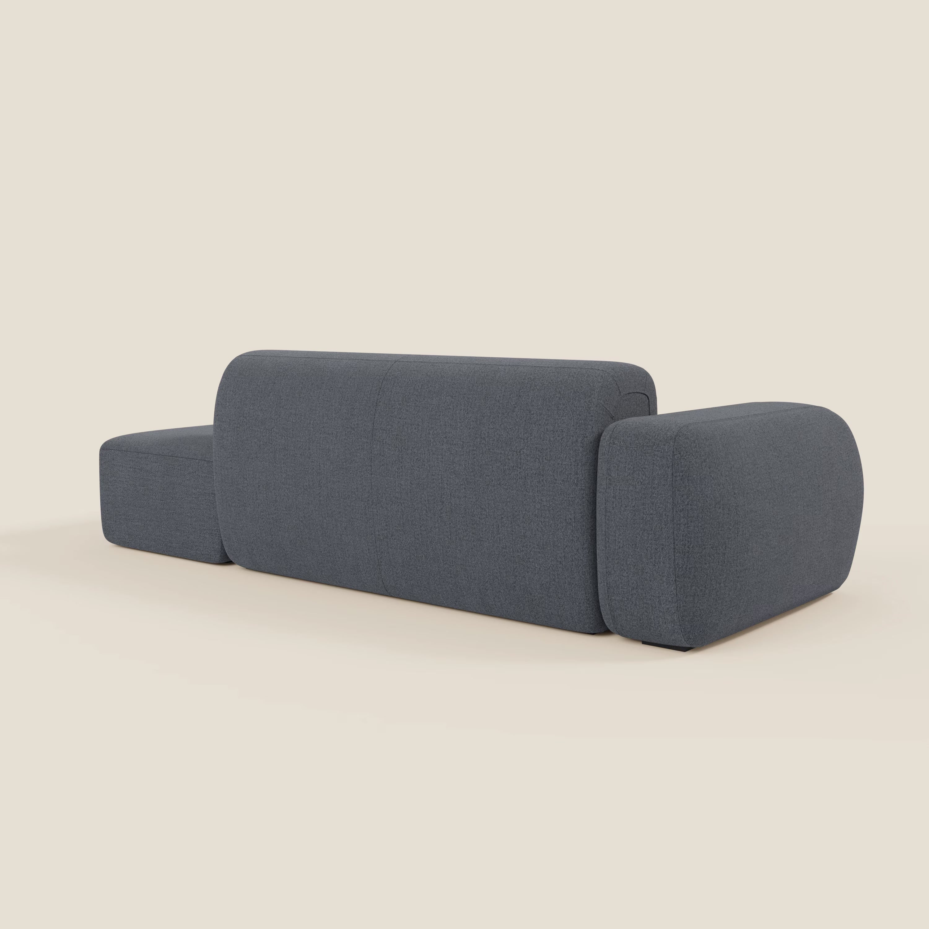 Il Divano componibile BonBon di Divani.Store è presentato dal retro in tessuto smacchiabile T23 blu grafite, caratterizzato da un design geometrico minimalista con bordi arrotondati, bracciolo spesso a blocchi, pouf terminale coordinato e sfondo beige chiaro.