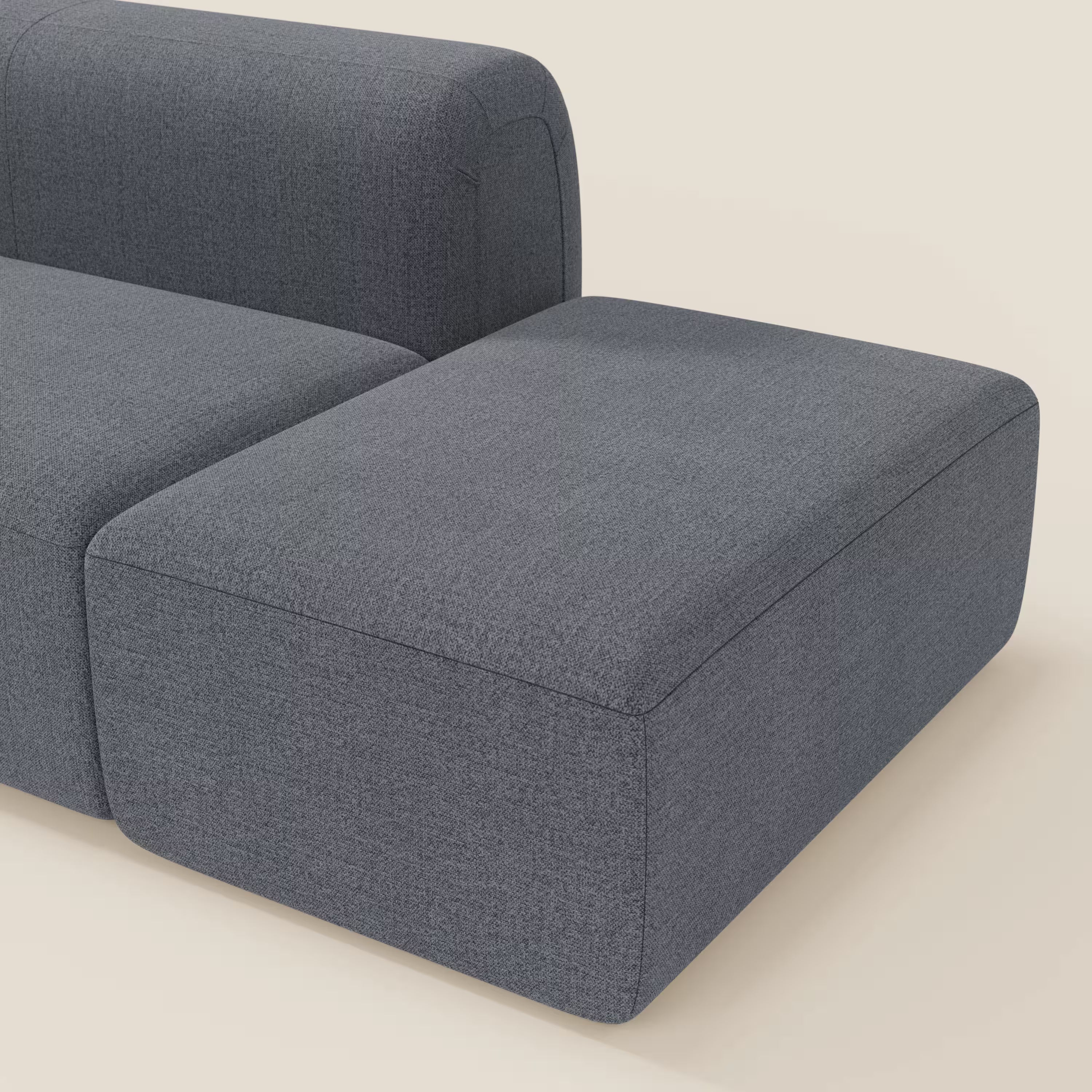 Primo piano del BonBon Divano componibile di Divani.Store in tessuto T23 blu grafite smacchiabile, che mostra le sue linee pulite, la forma squadrata e il pouf terminale con sezione angolare su uno sfondo beige chiaro.