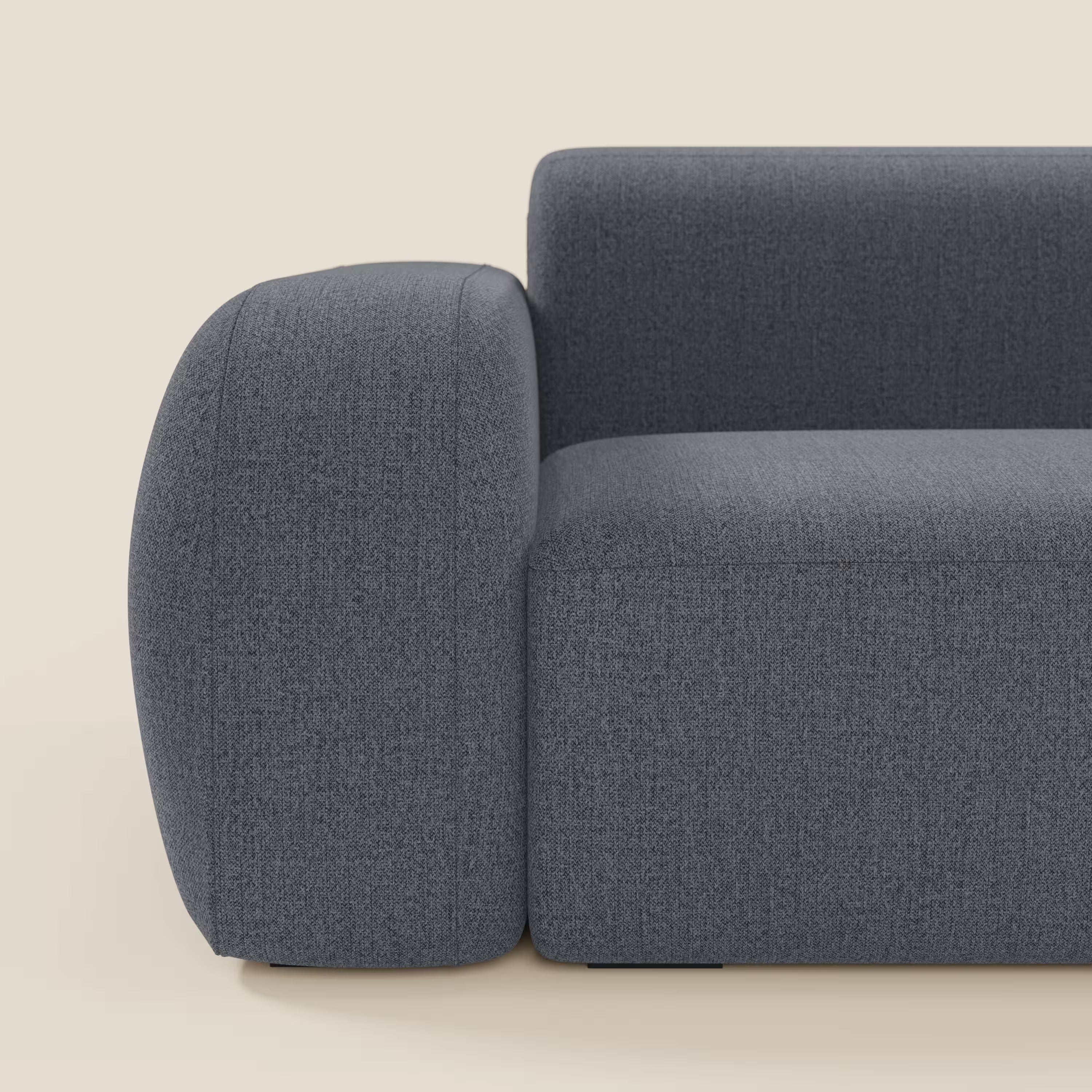 Primo piano di BonBon Divano componibile di Divani.Store in tessuto antimacchia T23 blu grafite, che mostra il bracciolo e la seduta arrotondati e morbidi, dalle linee pulite e minimaliste su uno sfondo beige chiaro.